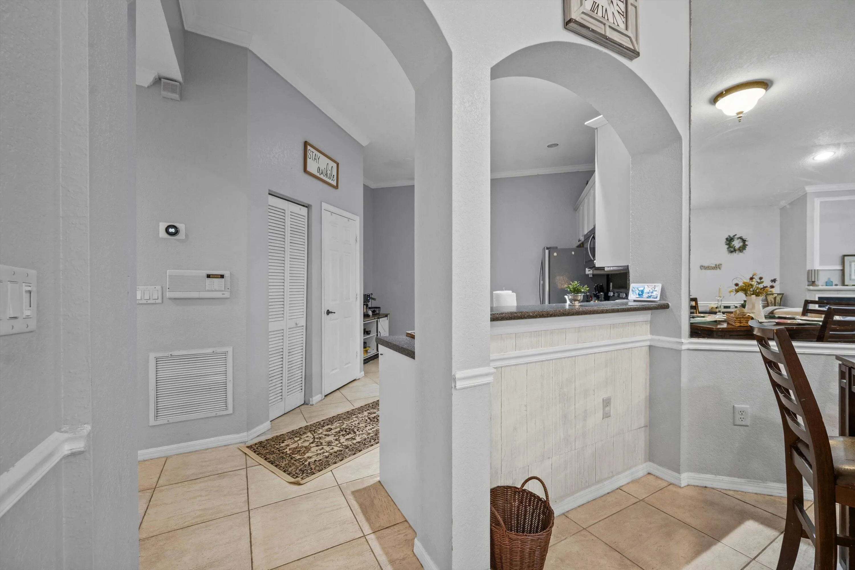 Arched entryway opening to a kitchen pass-through with a breakfast bar featuring a dark countertop and white paneling