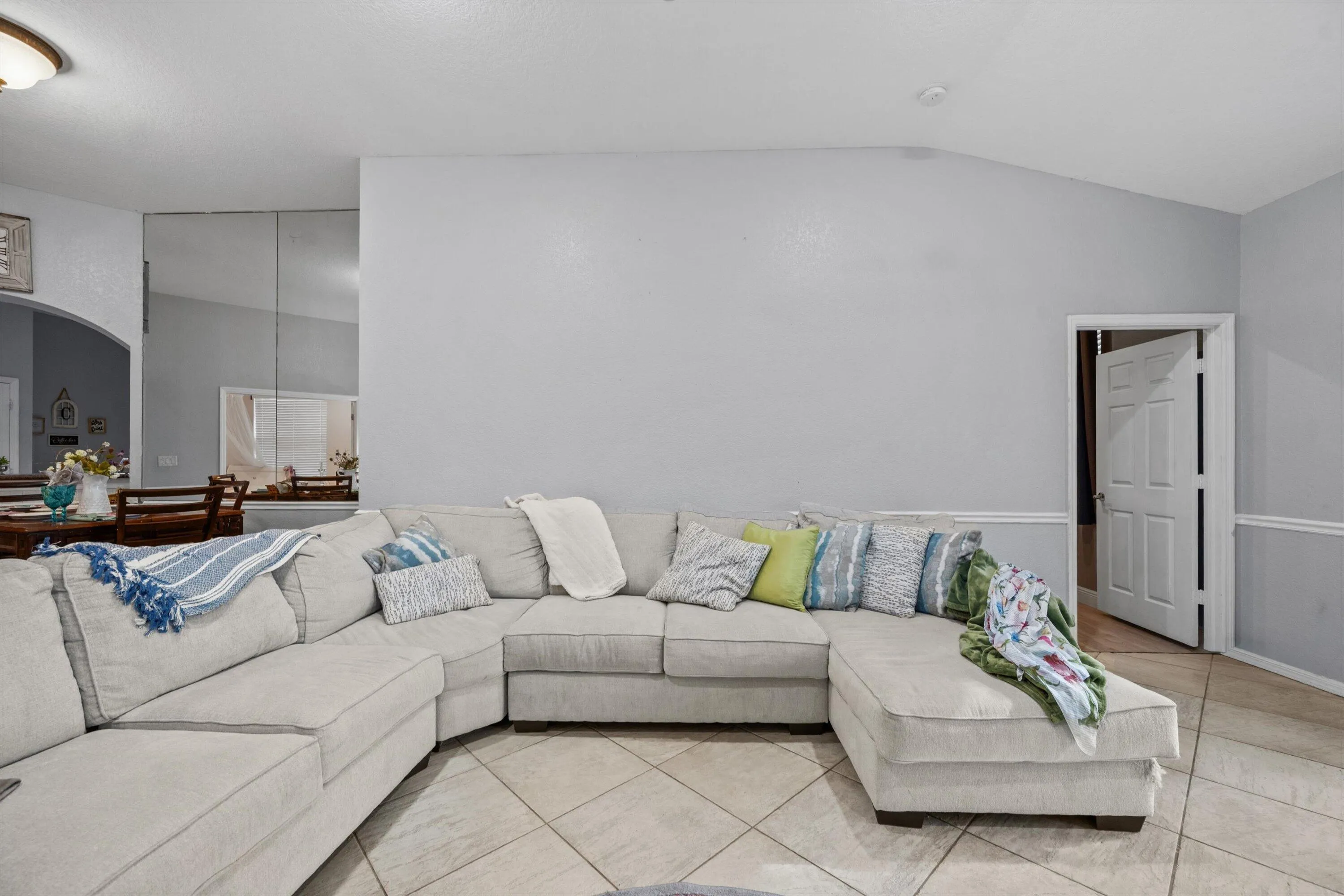 Spacious room featuring vaulted ceilings, light-toned tile flooring, and a chair rail molding