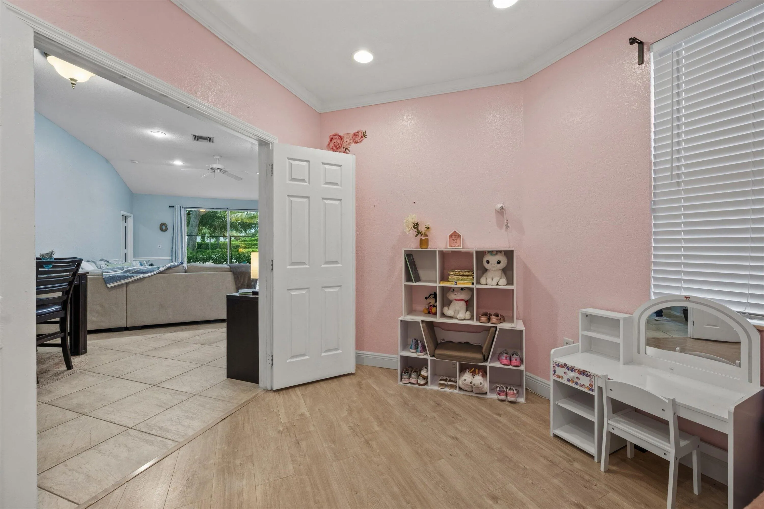 Recessed lighting and wood-finish flooring complement this versatile space, featuring a window with horizontal blinds and a white paneled door