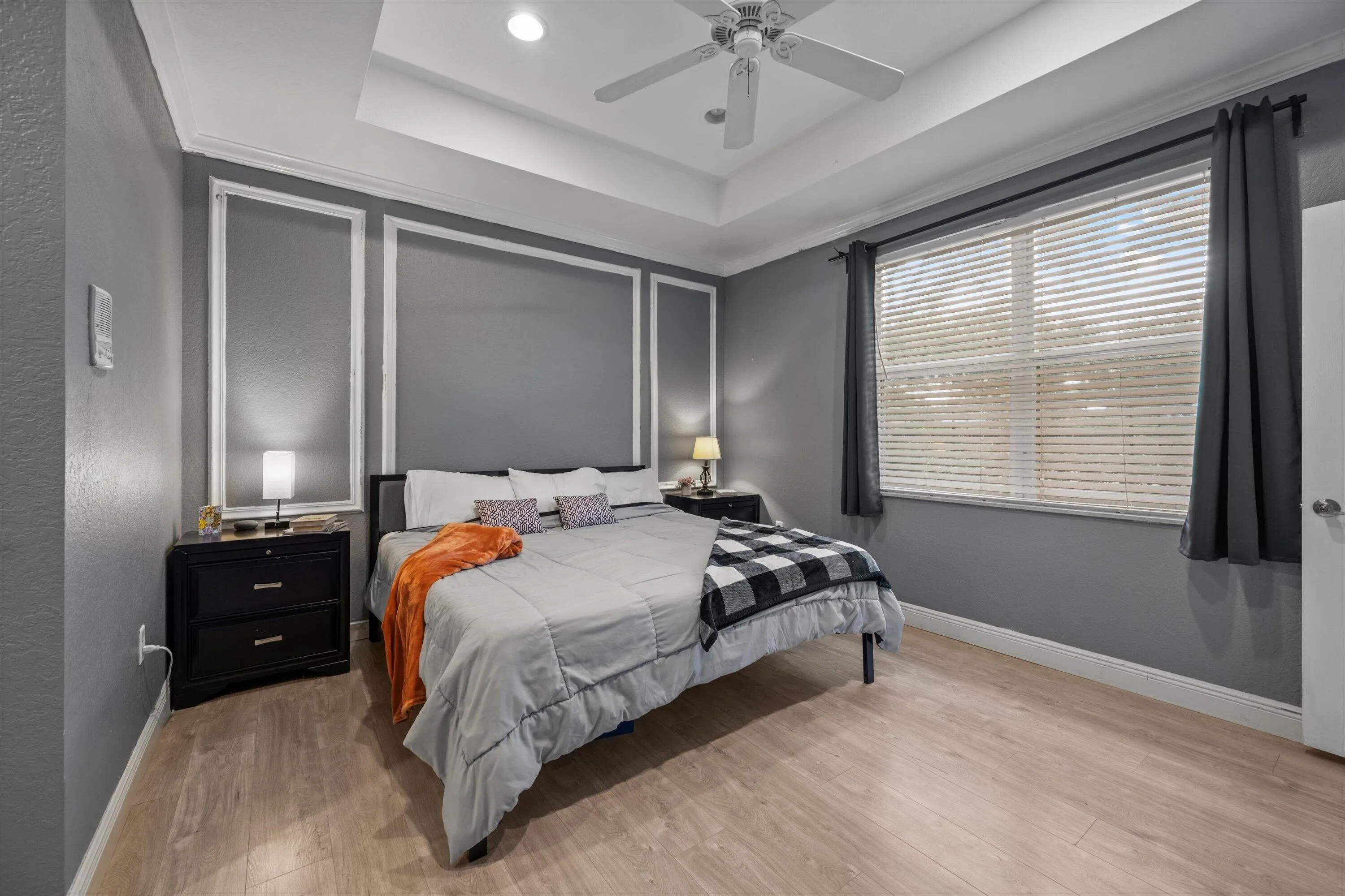Spacious room featuring tray ceiling, crown molding, wood-finish flooring, a ceiling fan, and a large window with blinds