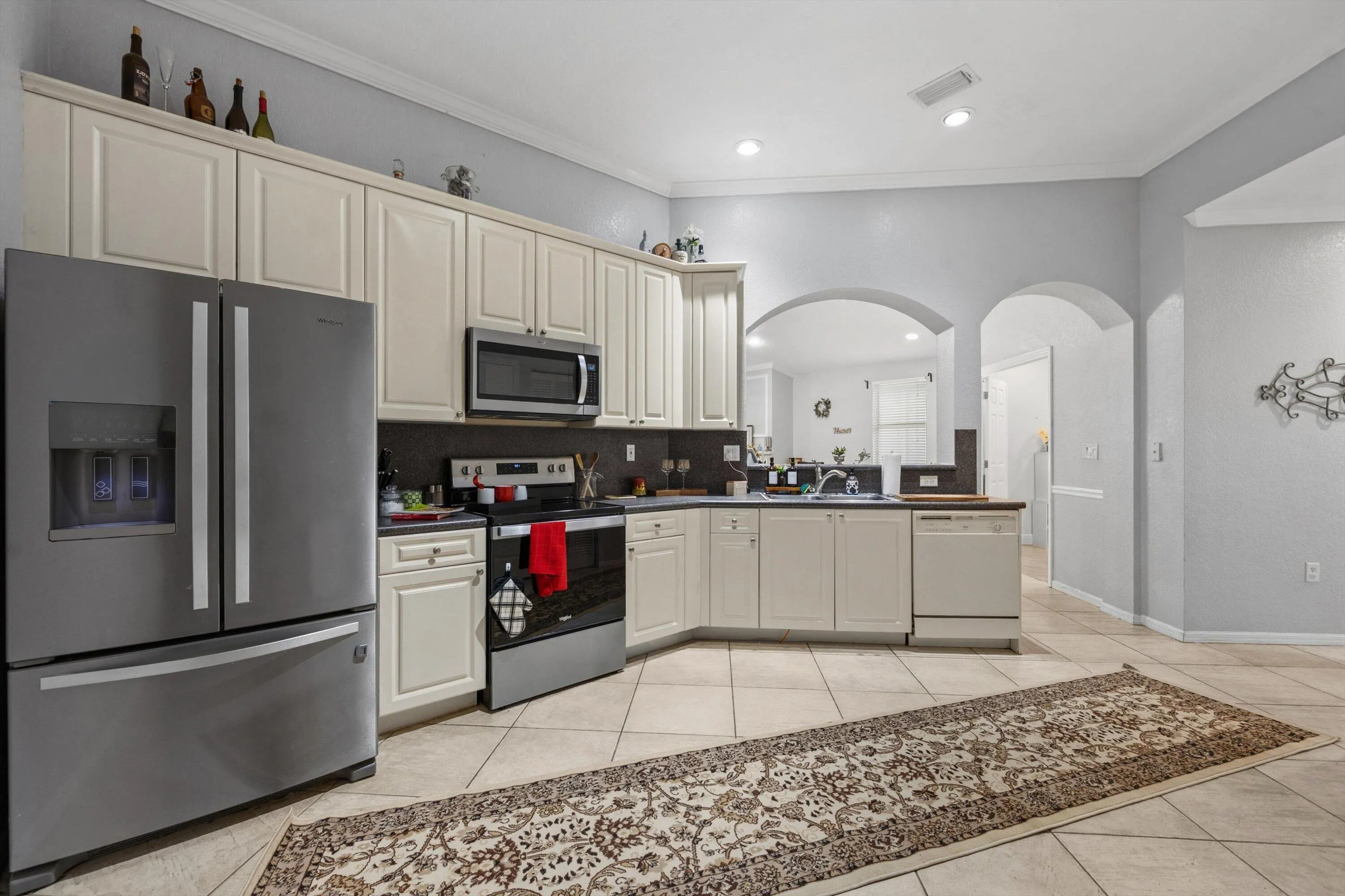 Kitchen featuring stainless steel appliances, light-toned cabinetry, tile flooring, and arched doorways