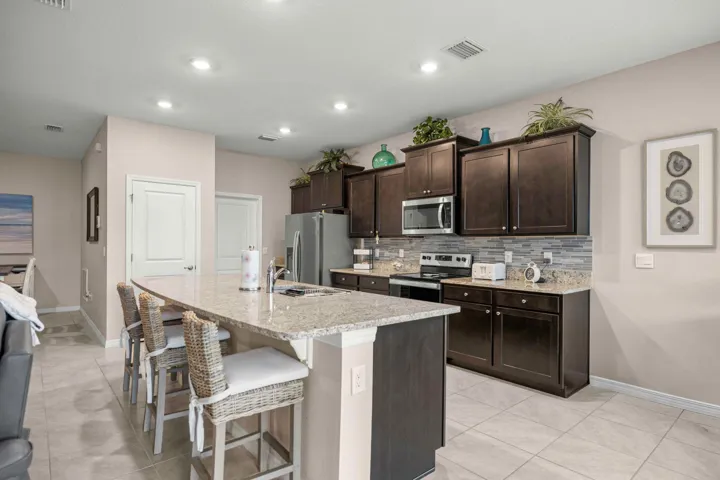 Spacious kitchen featuring an extended island with seating, granite countertops, dark wood-finish cabinetry, stainless steel appliances, and tile flooring
