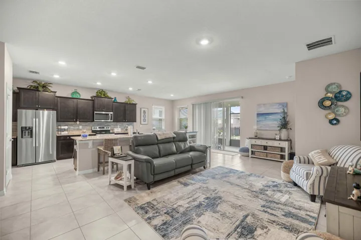Open-concept living space featuring ceramic tile flooring, recessed lighting, a kitchen with dark wood-finish cabinetry, stainless steel appliances, and a breakfast bar