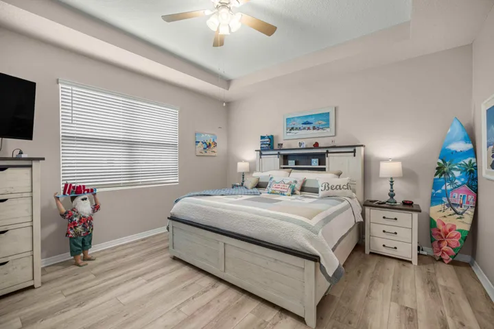 Bedroom featuring light wood-finish flooring, a tray ceiling, and a ceiling fan with integrated lighting