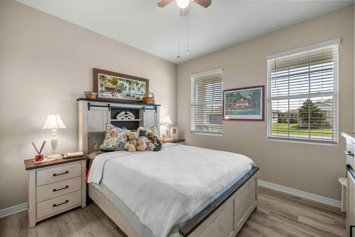 Bedroom featuring wood-finish flooring, two windows with blinds, and a ceiling fan with light fixture