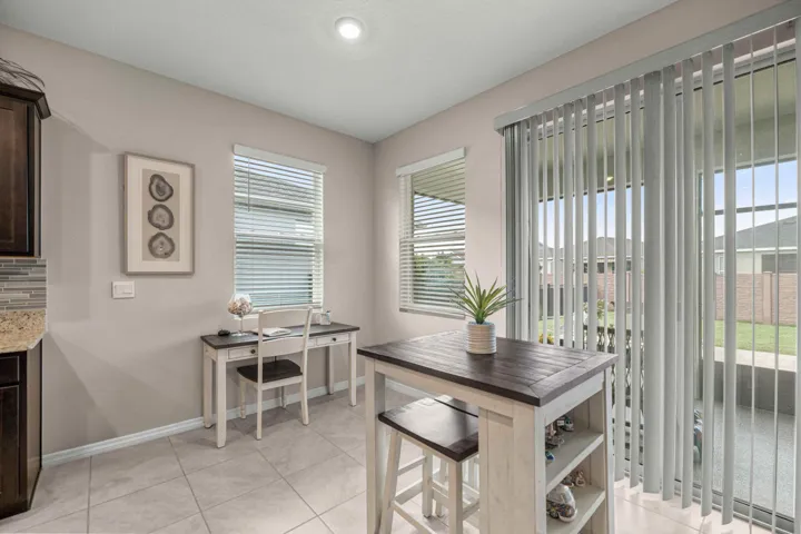 Tiled flooring throughout this bright space, featuring a built-in desk area, a kitchen island with integrated shelving, and vertical blinds covering the sliding glass door