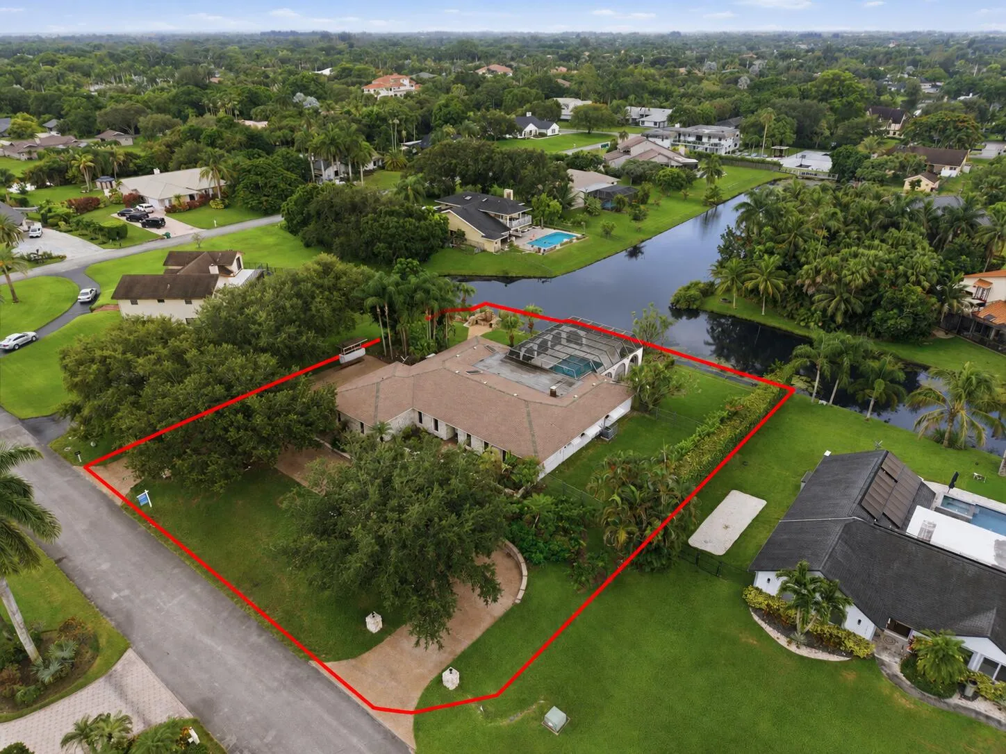 Waterfront property featuring a private pool enclosure, expansive lot, mature landscaping, and a paver driveway