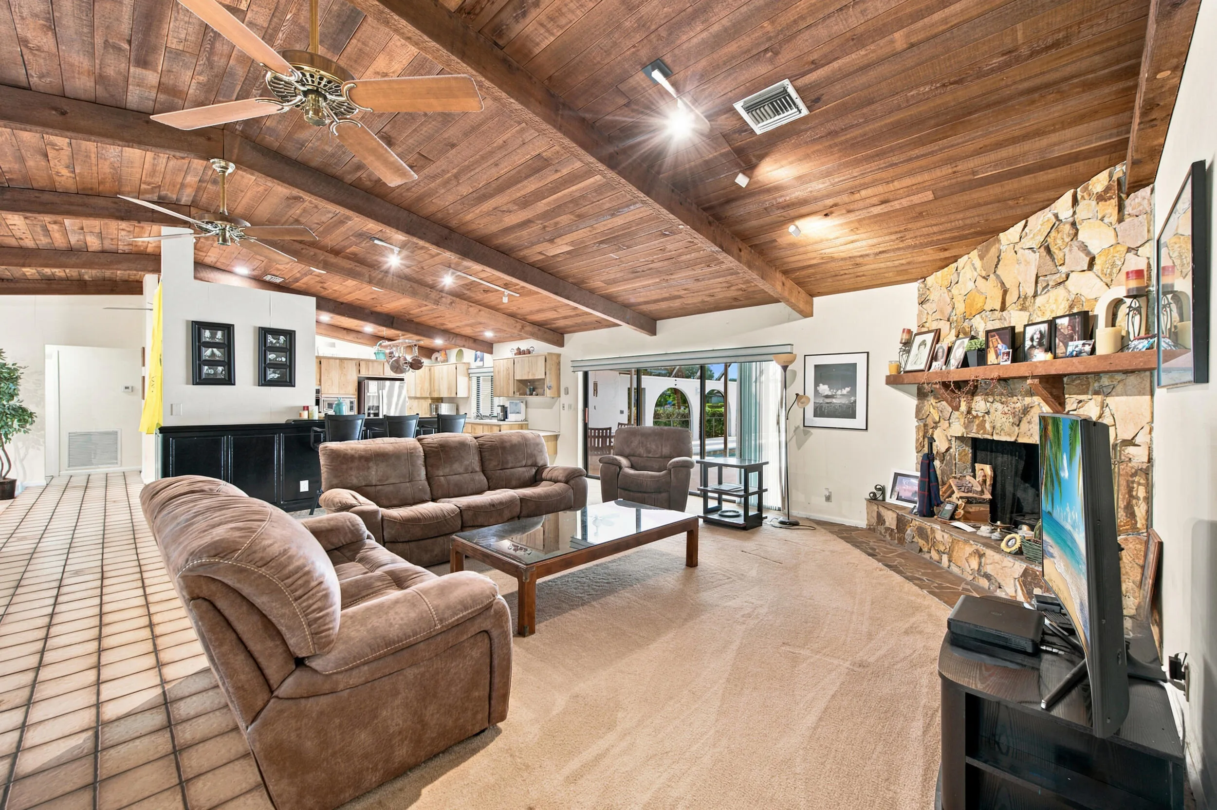 Vaulted wood-plank ceiling with exposed beams, stone-clad fireplace with mantel, tiled flooring, track lighting, and recessed lighting