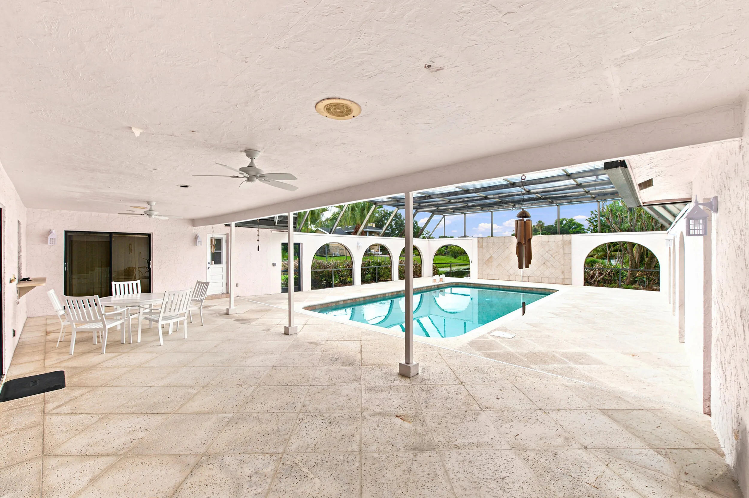 Expansive outdoor living area featuring a rectangular pool, covered patio, screened enclosure, and stone tile flooring