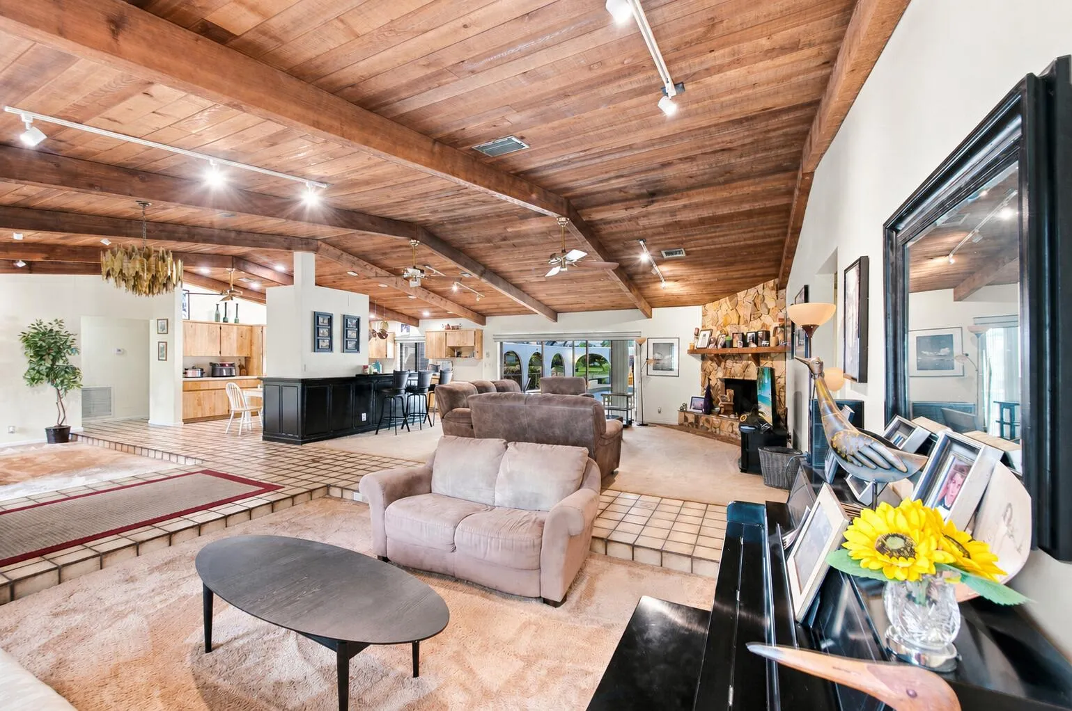 Open-concept living area featuring a vaulted wood-paneled ceiling with exposed beams, track lighting, and ceiling fans