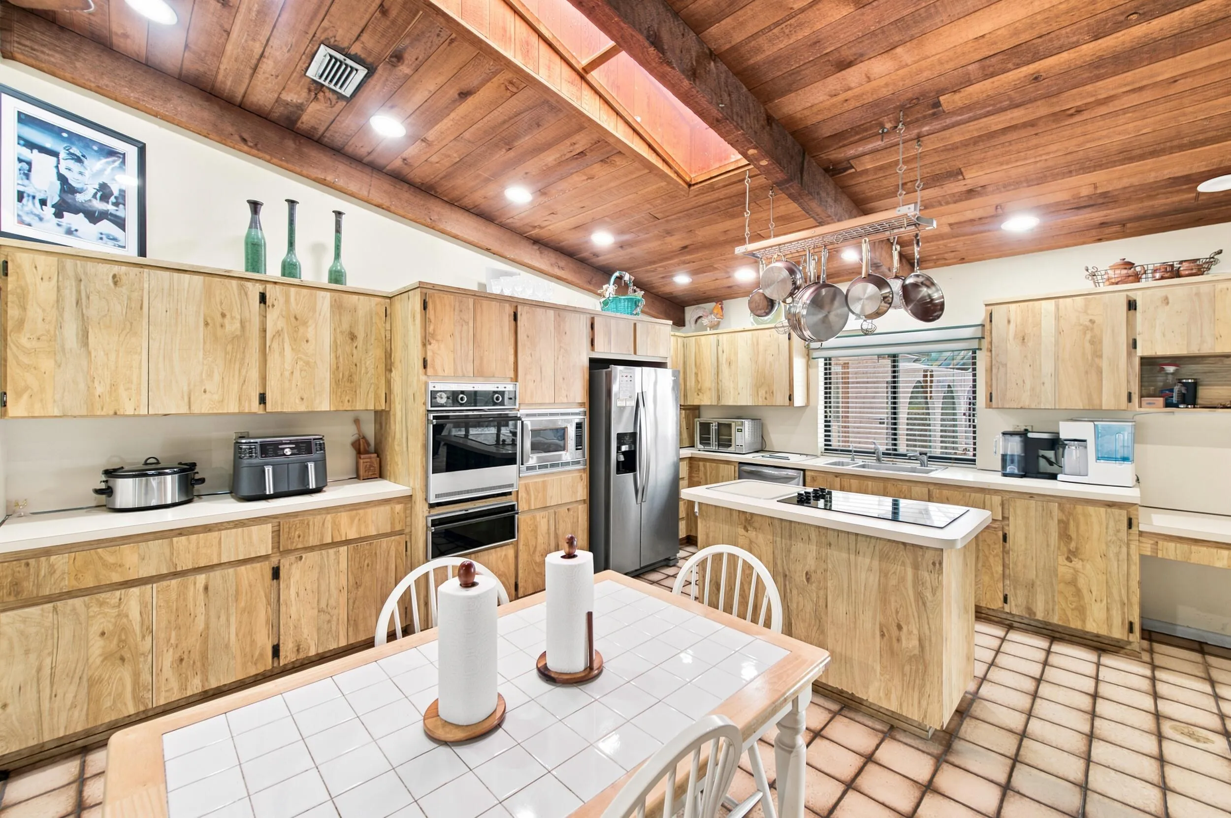 Kitchen featuring a wood-panel vaulted ceiling with recessed lighting, extensive wood-finish cabinetry, built-in double ovens, and a center island with a cooktop