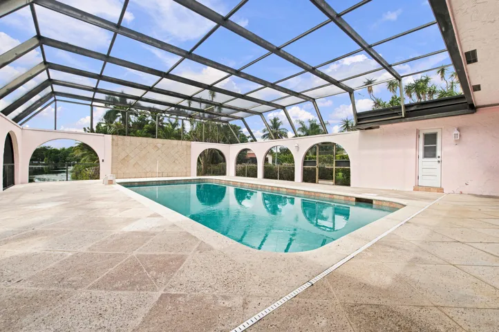 Screen-enclosed pool area featuring a blue-tiled swimming pool, expansive paved decking, and arched openings