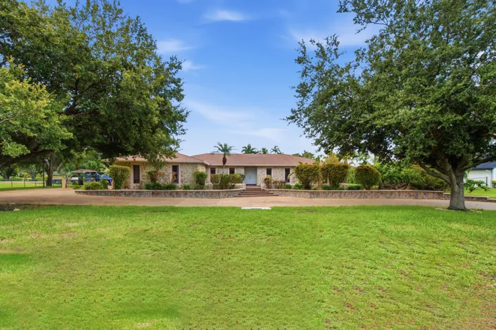 Expansive front lawn with mature shade trees leading to a stone-clad facade residence