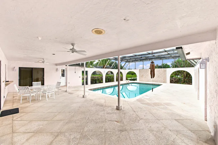 Expansive outdoor living area featuring a rectangular pool, covered patio, screened enclosure, and stone tile flooring