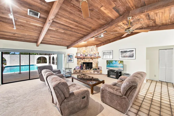 Vaulted wood-plank ceiling with exposed beams, stone-faced fireplace, large sliding glass doors, screened patio, and a swimming pool