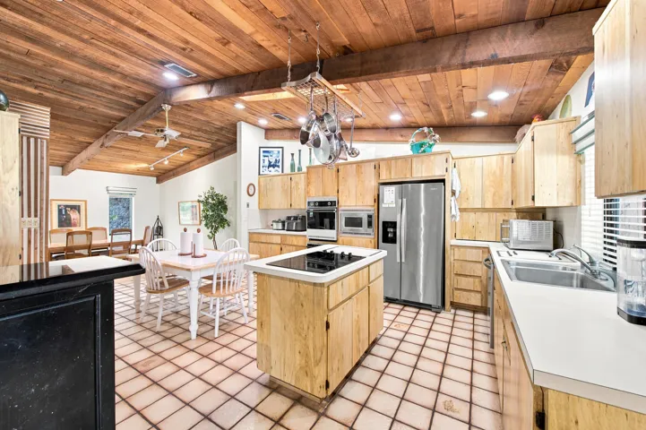 Open-concept kitchen featuring wood-finish cabinetry, a centered island with an integrated cooktop, stainless steel appliances, and a tile floor
