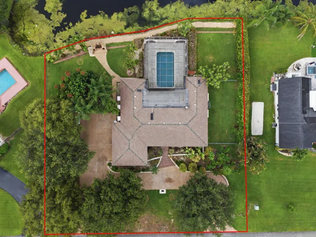 Expansive property featuring a screened swimming pool, paved driveway, mature trees, and waterfront access with a decorative gazebo