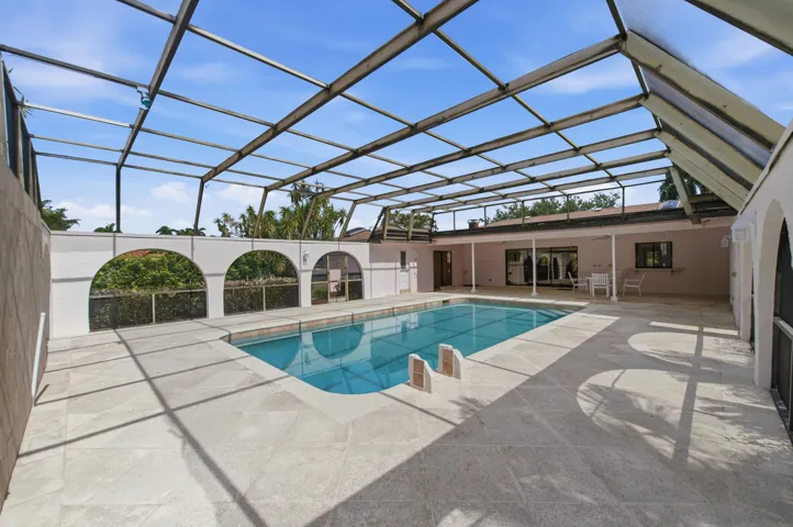 Screen-enclosed pool area featuring a rectangular swimming pool, expansive paved decking, and arched wall details
