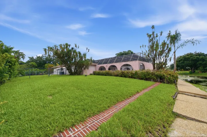 Expansive green lawn with a brick-lined path, leading towards a residence featuring arched window openings and a screened enclosure