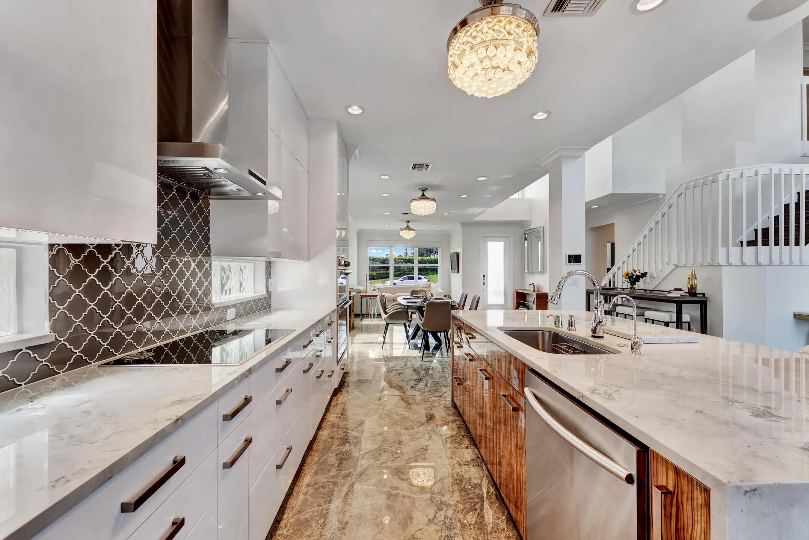 Long view down the gourmet kitchen showing the oversized island with prep sink, dishwasher, and open flow to the dining area.