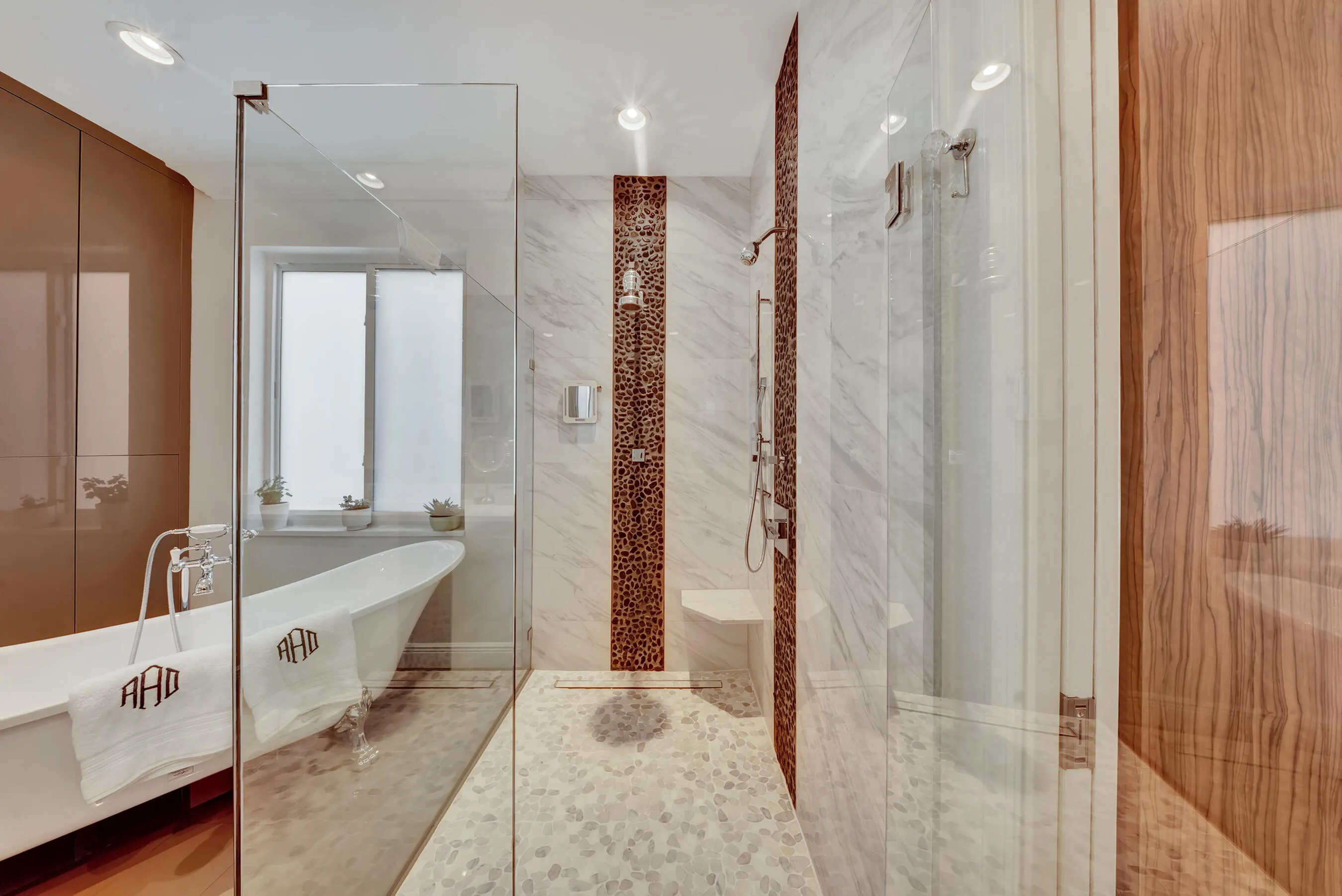 Spa-style primary bathroom with freestanding soaking tub, frameless glass walk-in shower, and pebble-stone accents.