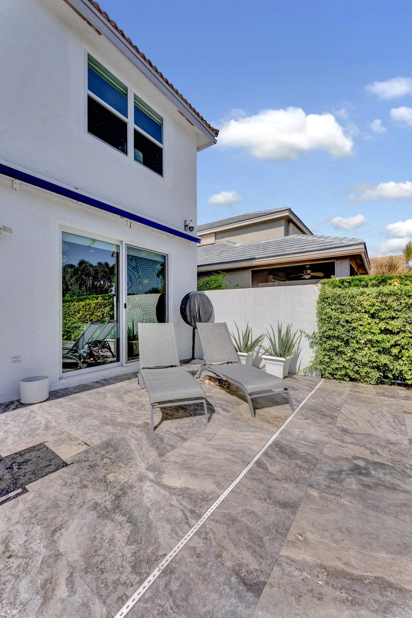 Travertine sun deck with loungers, privacy hedge walls, and tropical landscaping.