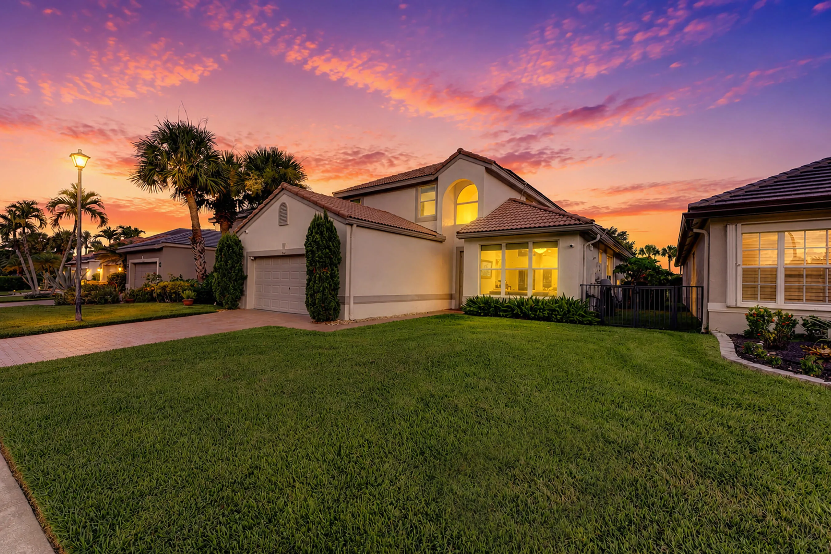Sunset exterior across the sweeping front lawn with illuminated windows and landscape lighting.