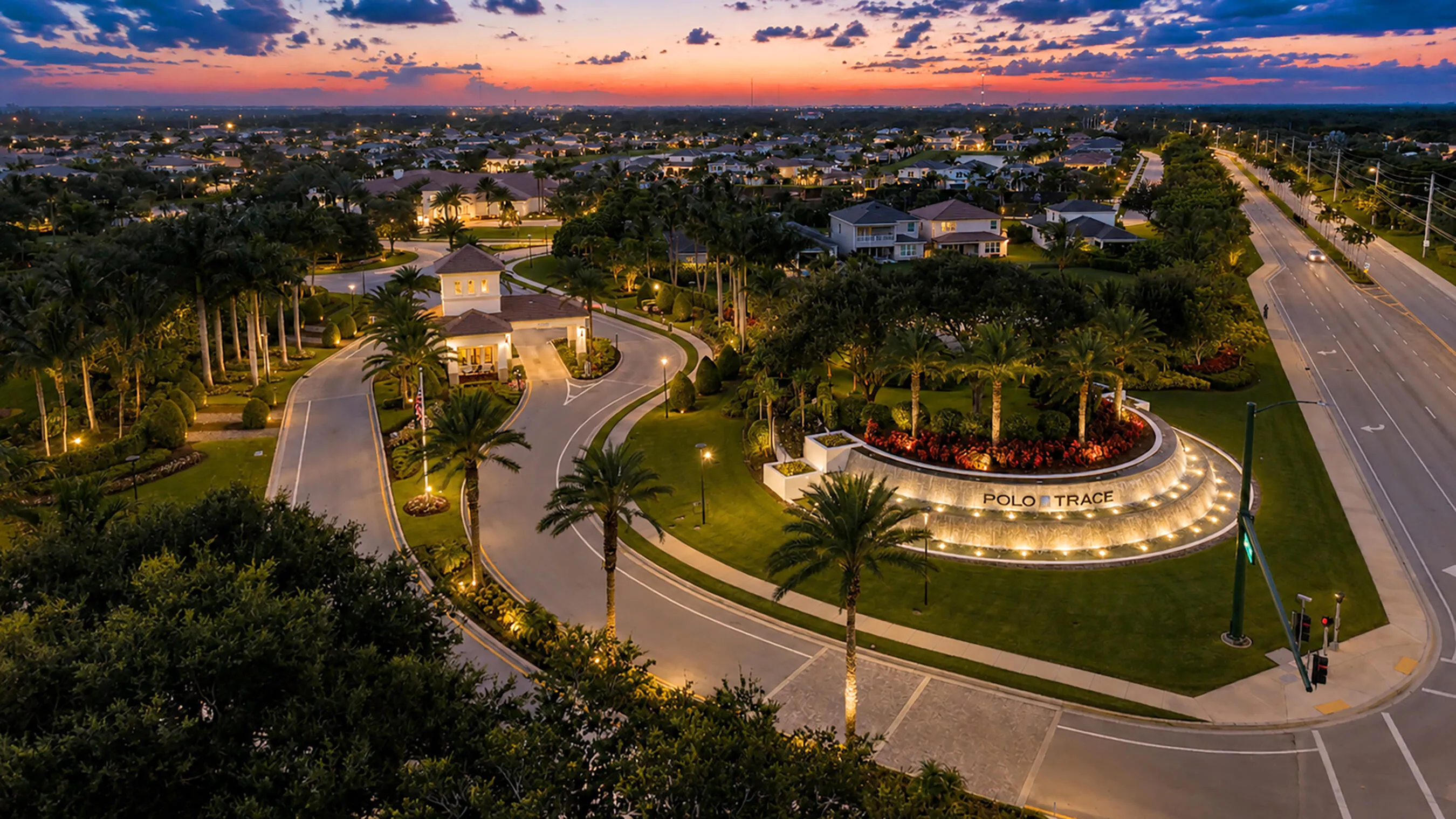Illuminated Polo Trace entrance at twilight with waterfall monument, royal palms, and manicured gardens.