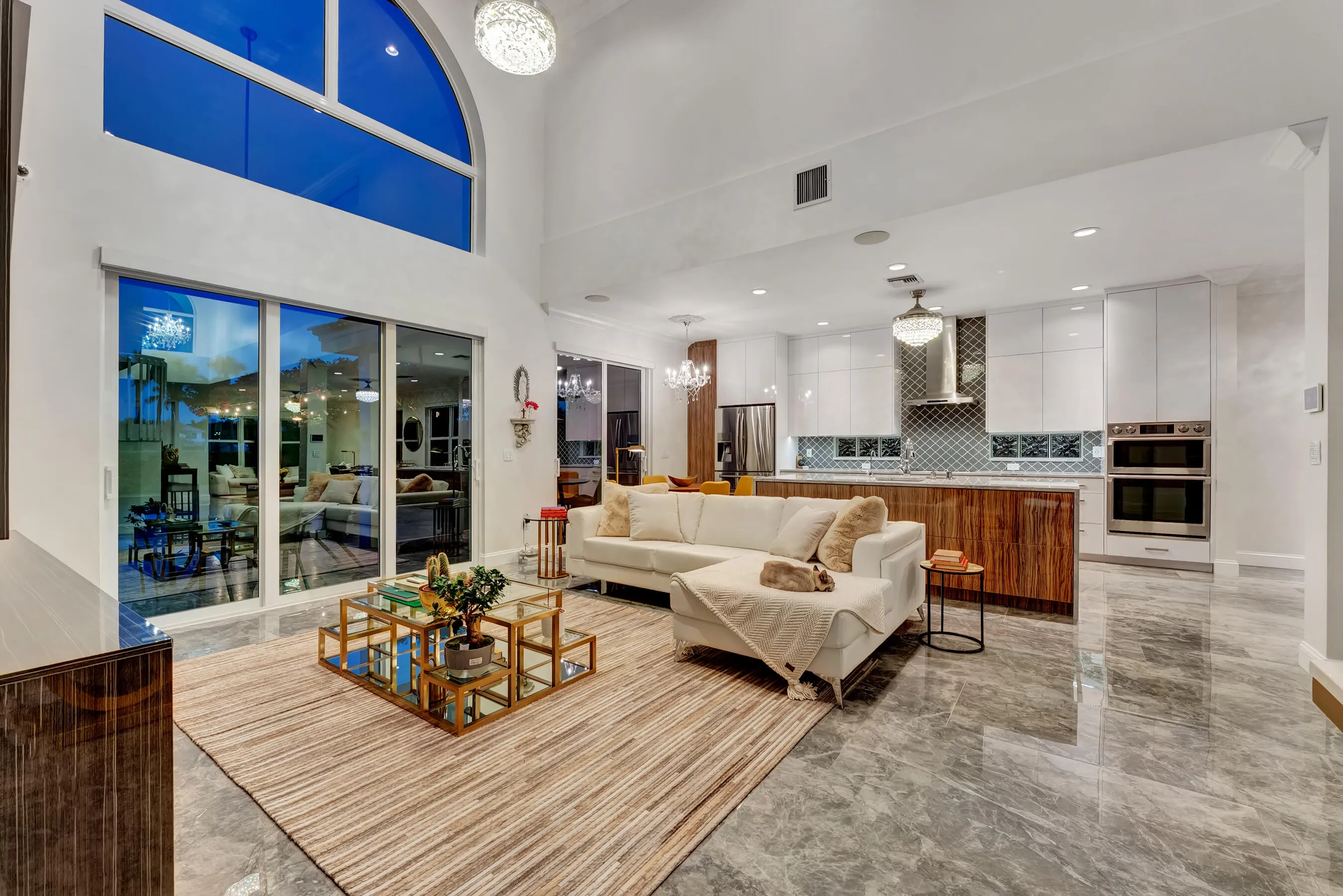 Great room at evening with two-story arched window framing the deep blue twilight sky.