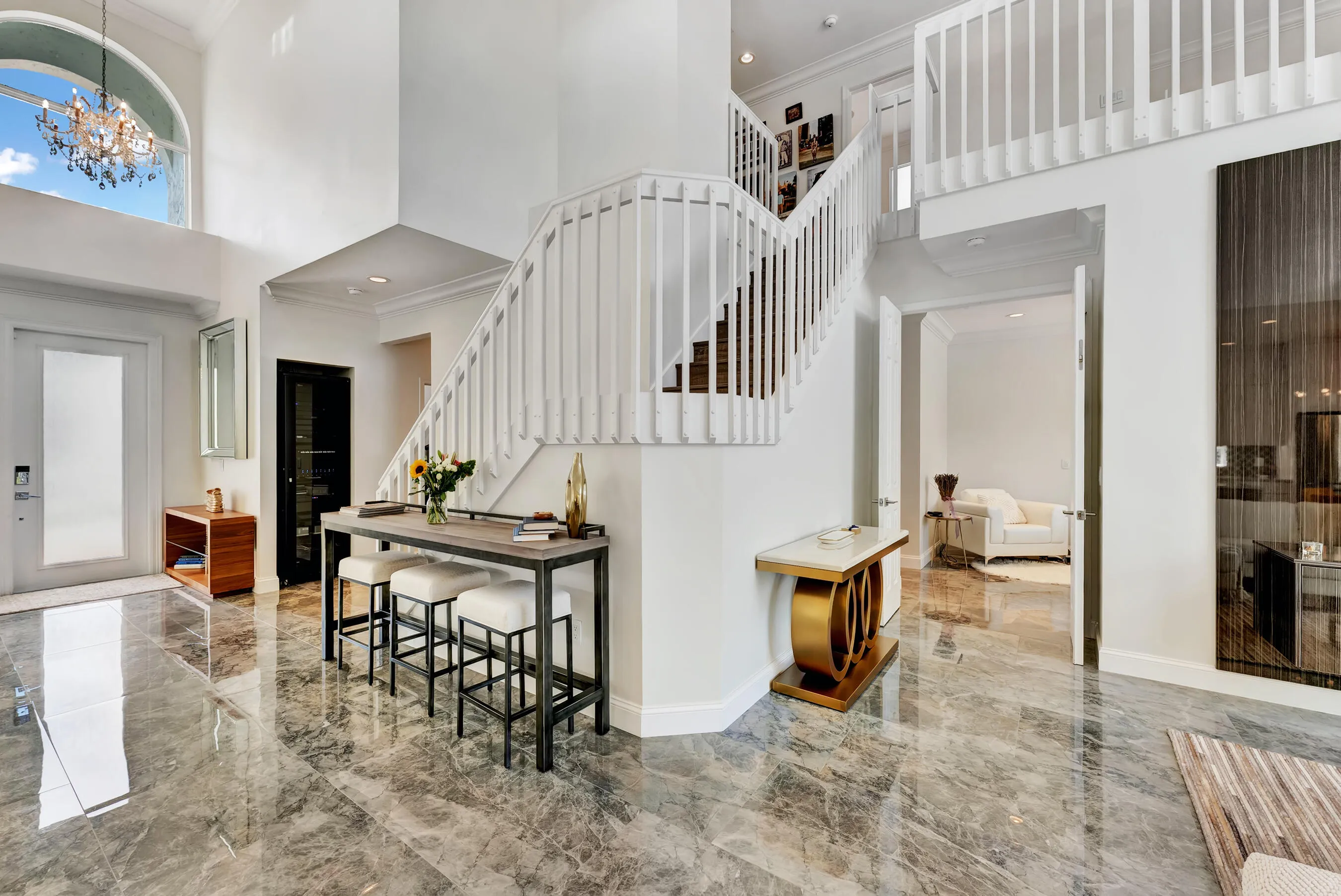 Bright foyer with polished marble-look tile floors, white staircase, and breakfast bar seating in the open-concept main living area.