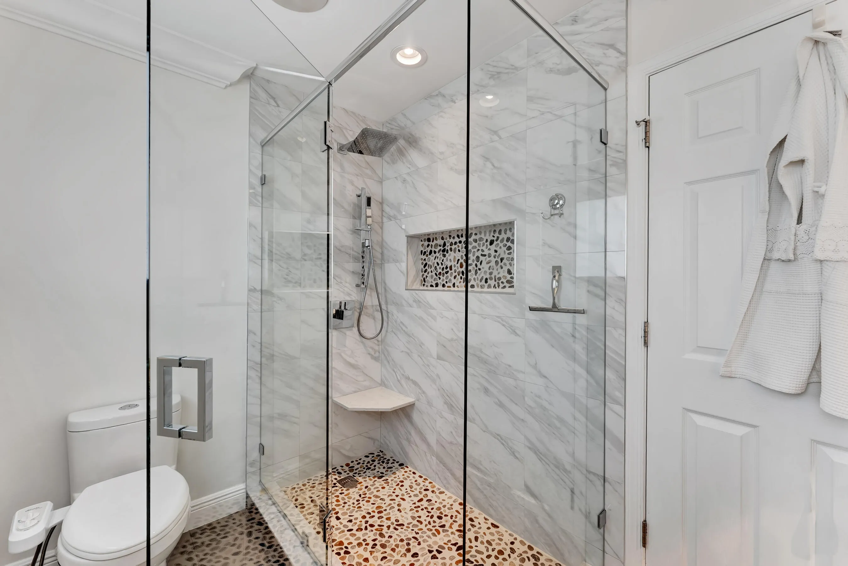 Upstairs bath with frameless glass walk-in shower, marble-look tile, and pebble accent flooring.