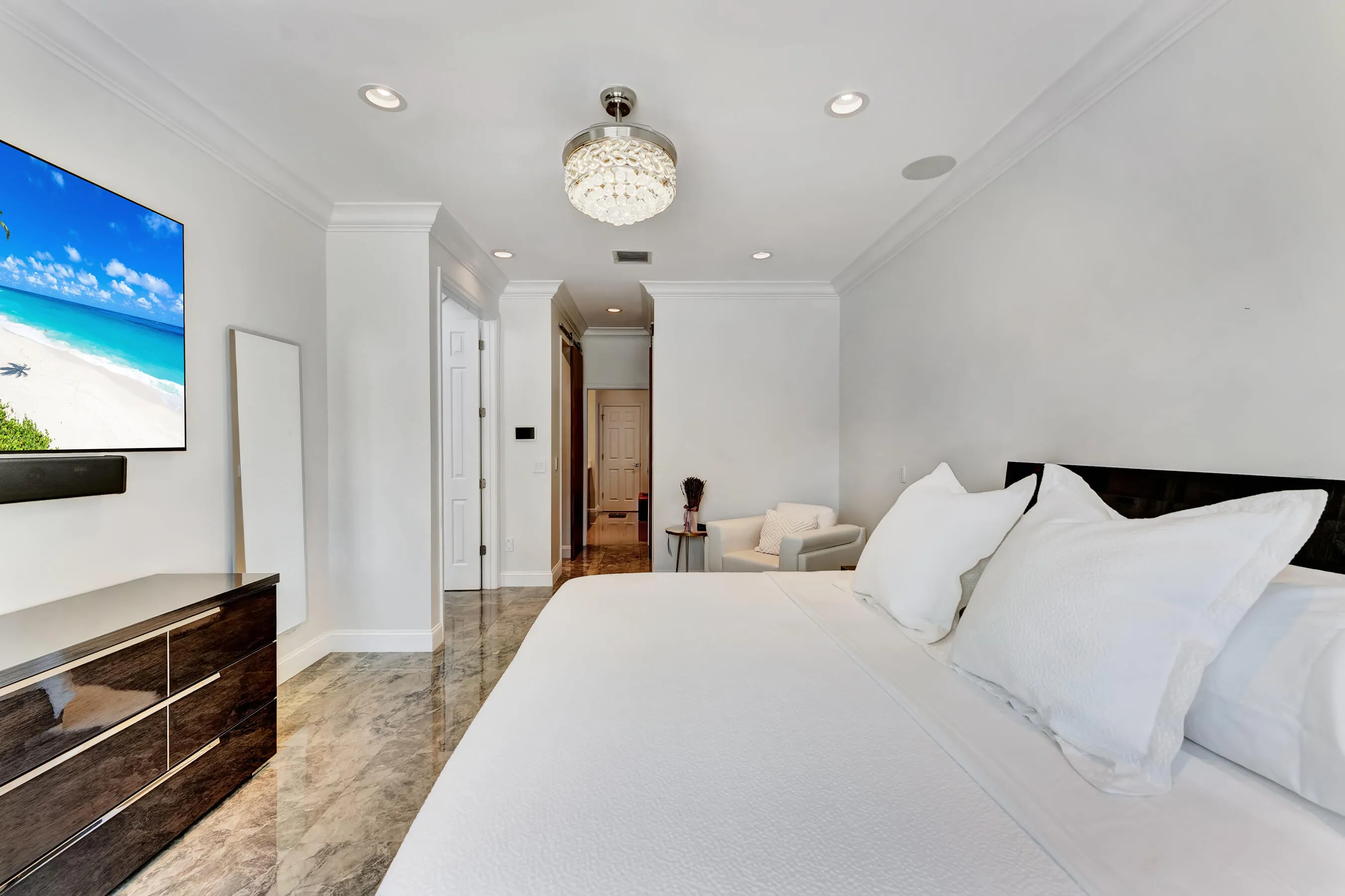 Spacious primary bedroom with king bed, custom furnishings, and marble-look tile flooring.