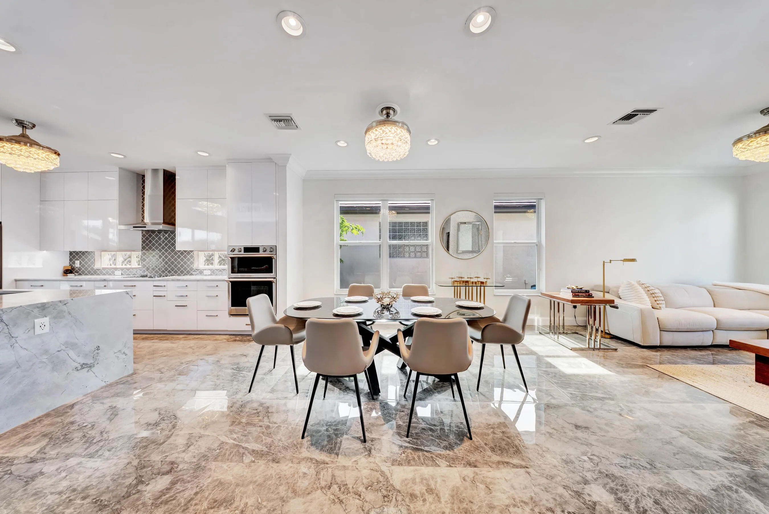 Wide view of the open-concept main level — kitchen, dining, and living areas with polished tile floors and designer lighting throughout.