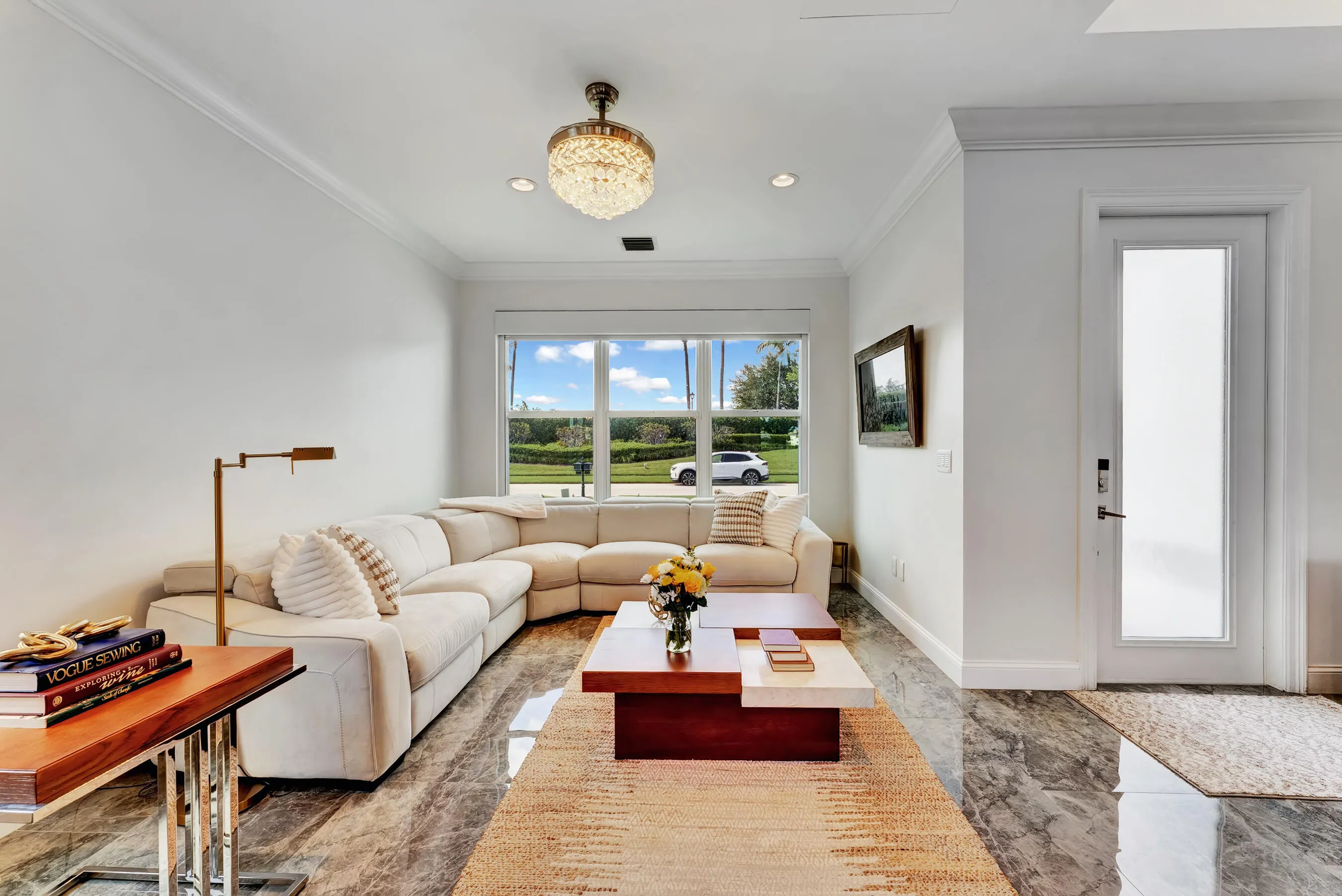 Formal living room with oversized sectional, designer lighting, crown molding, and views of the front lawn.