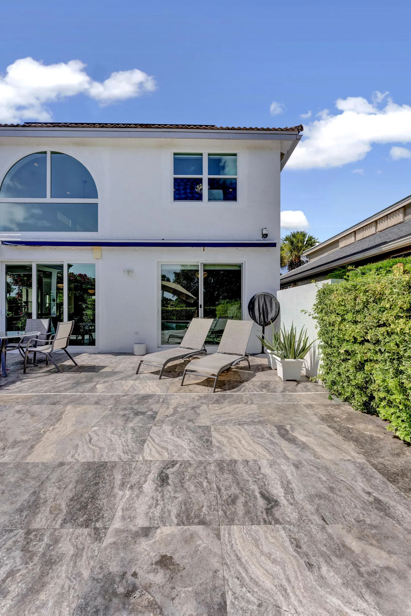 Expansive travertine rear patio with lounge seating below the home's two-story rear elevation.