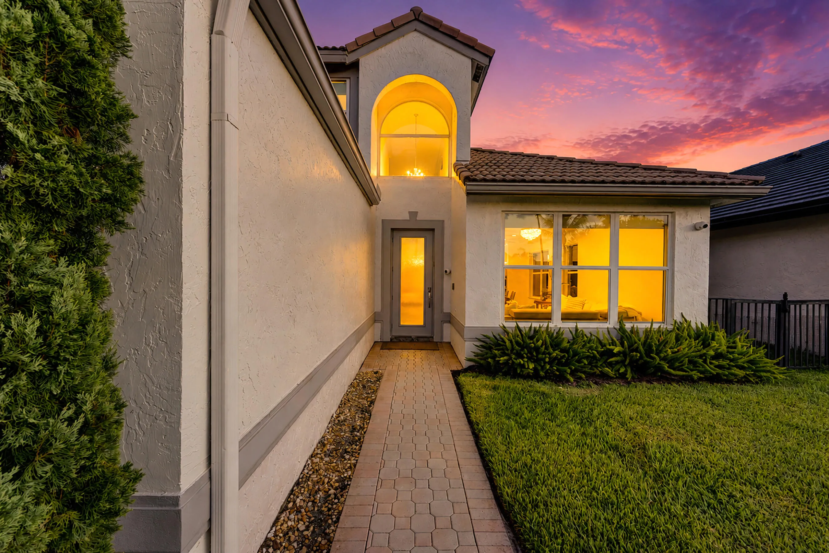 Front entry walkway at dusk with the arched two-story window glowing above.