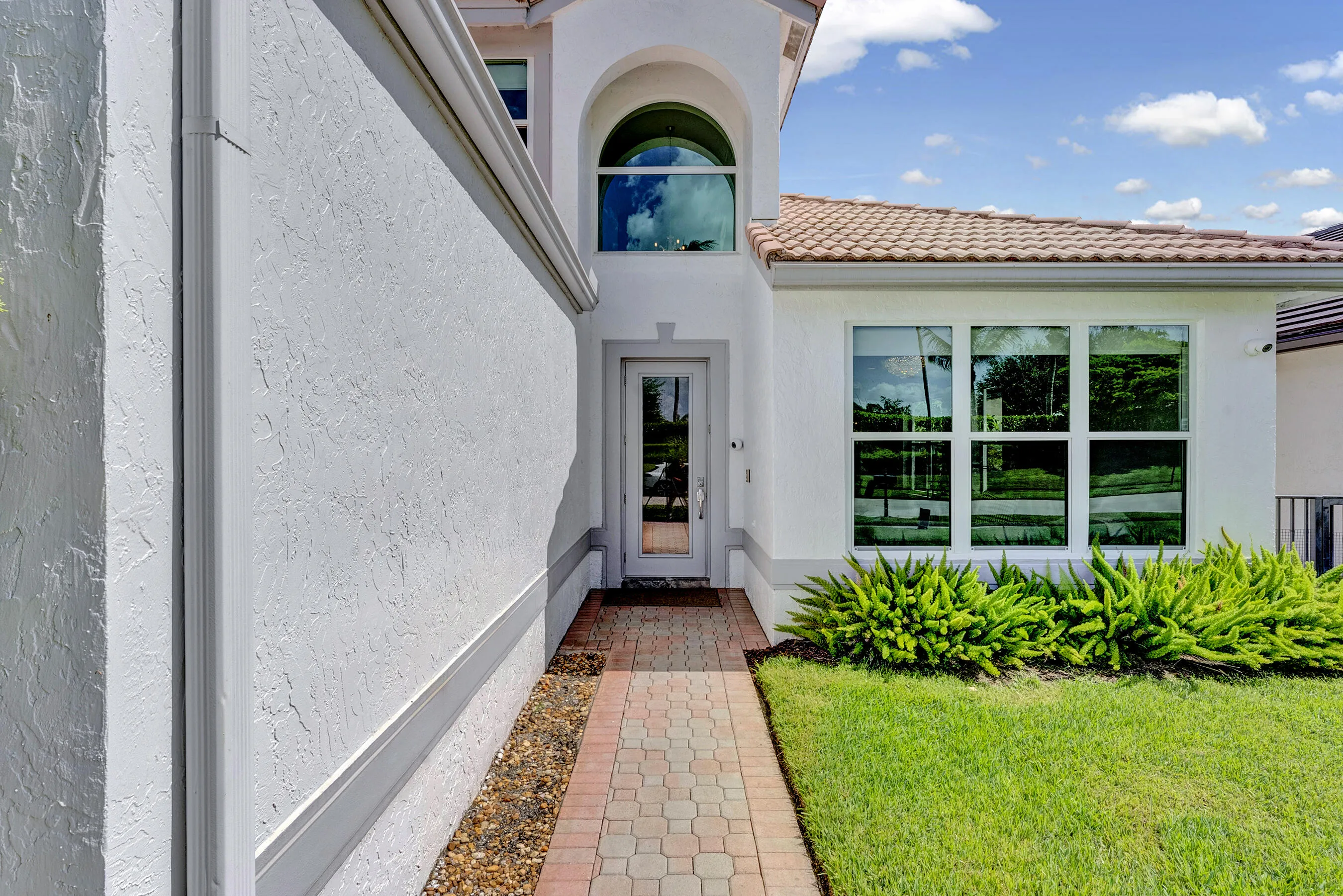Paver walkway leading to the front entry beneath a dramatic two-story arched window.