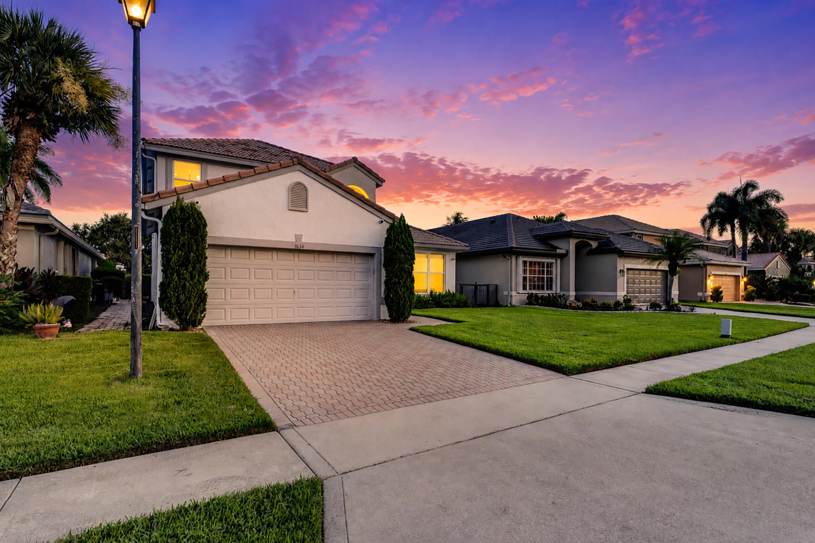Twilight view of the paver driveway and glowing front exterior under a vivid Florida sunset sky.