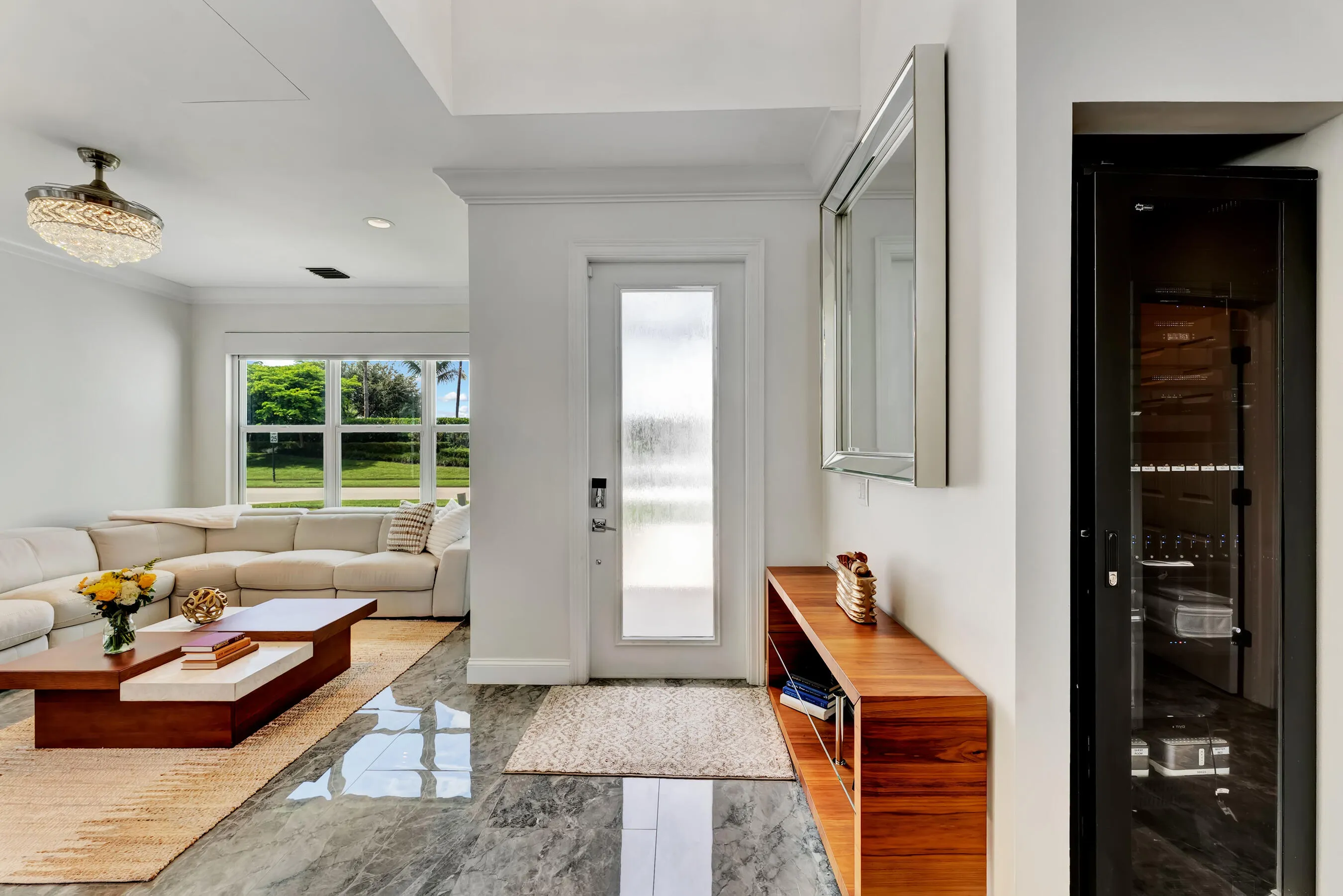 Living room looking toward the glass-paneled front door, with gleaming tile floors and abundant natural light.