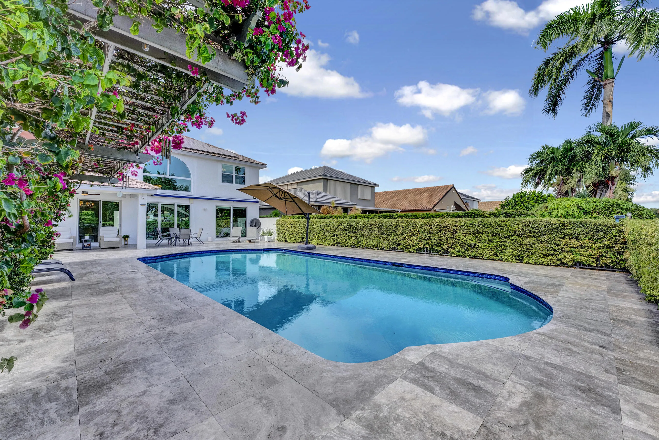 Resort-style pool framed by a bougainvillea-draped pergola in full bloom — true South Florida outdoor living.