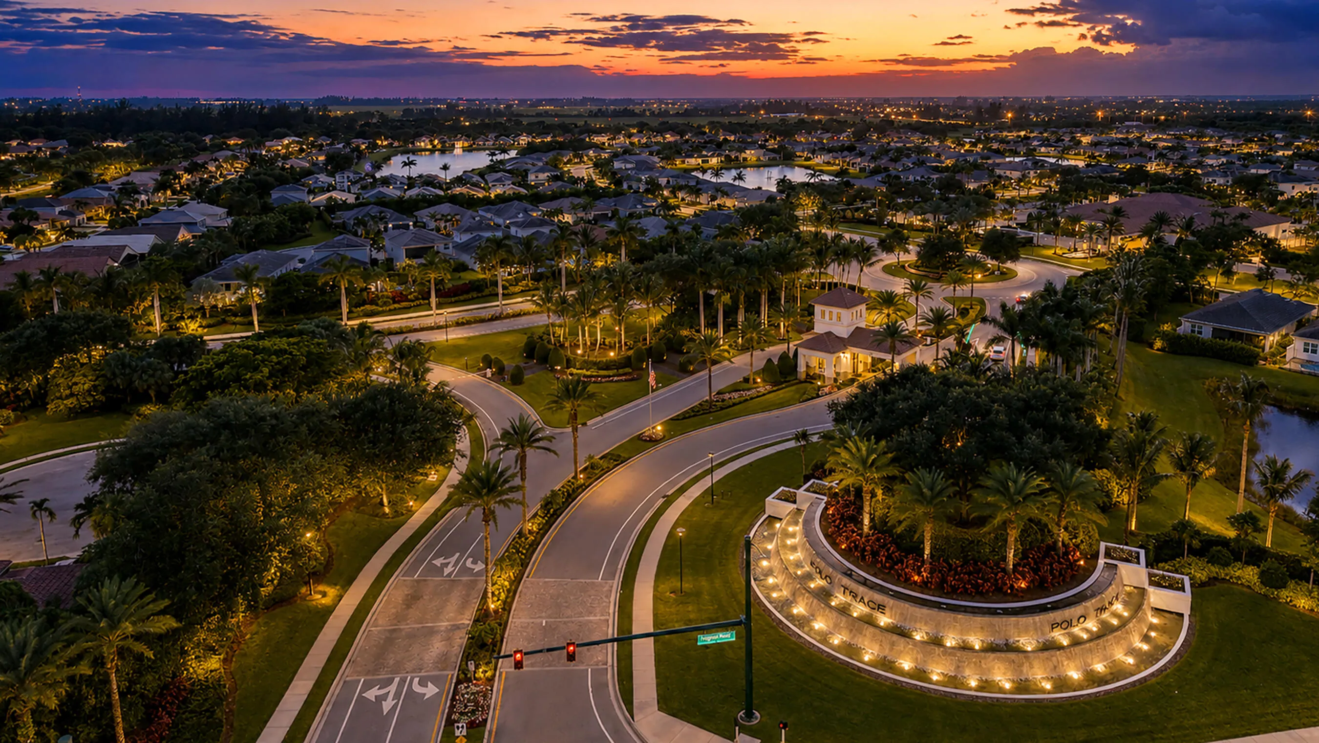 High twilight aerial above the gated Polo Trace entrance with the lake community glowing beyond — the final word in Delray Beach lifestyle.