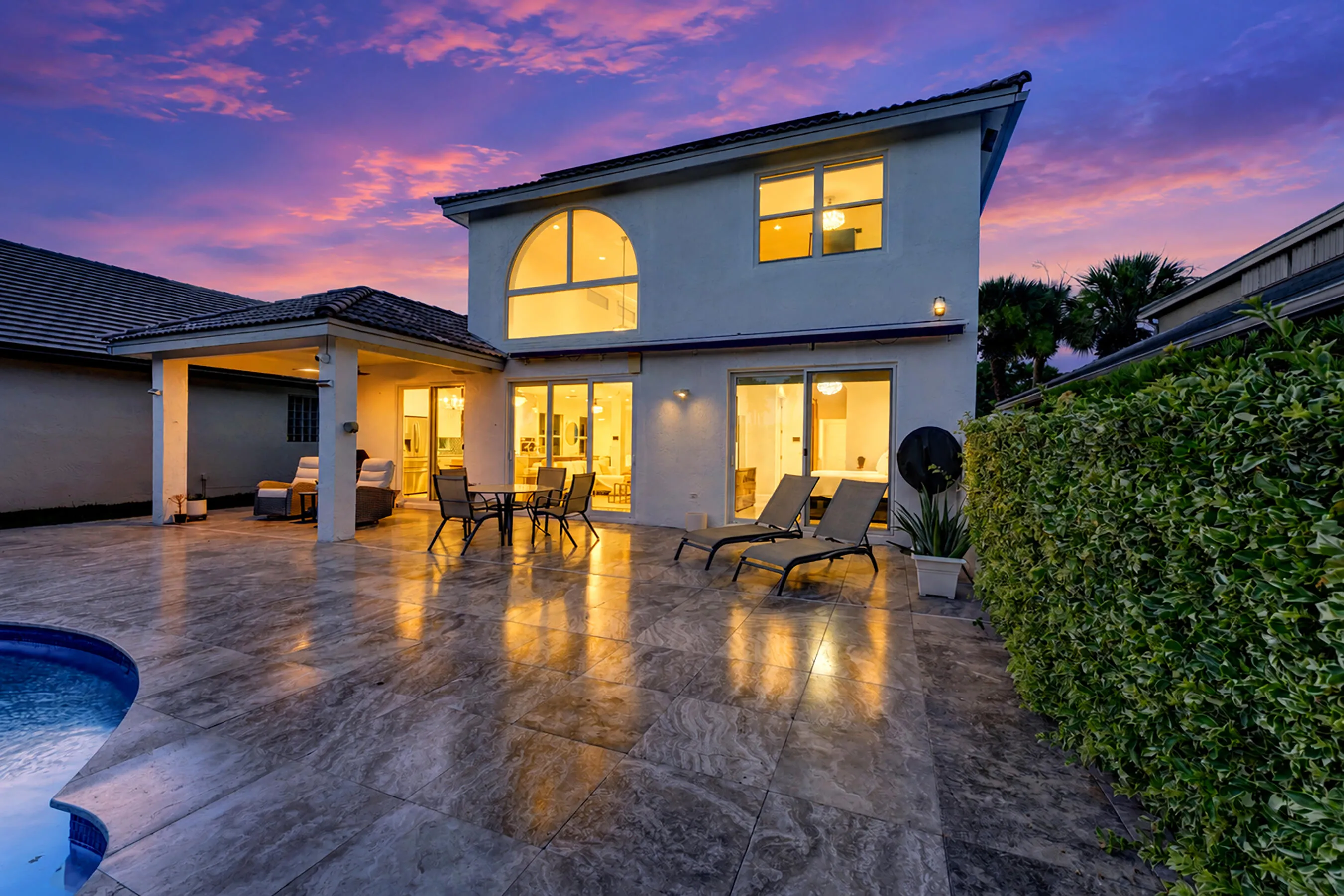 Rear elevation at twilight showing the covered patio, outdoor dining, and glowing interiors.
