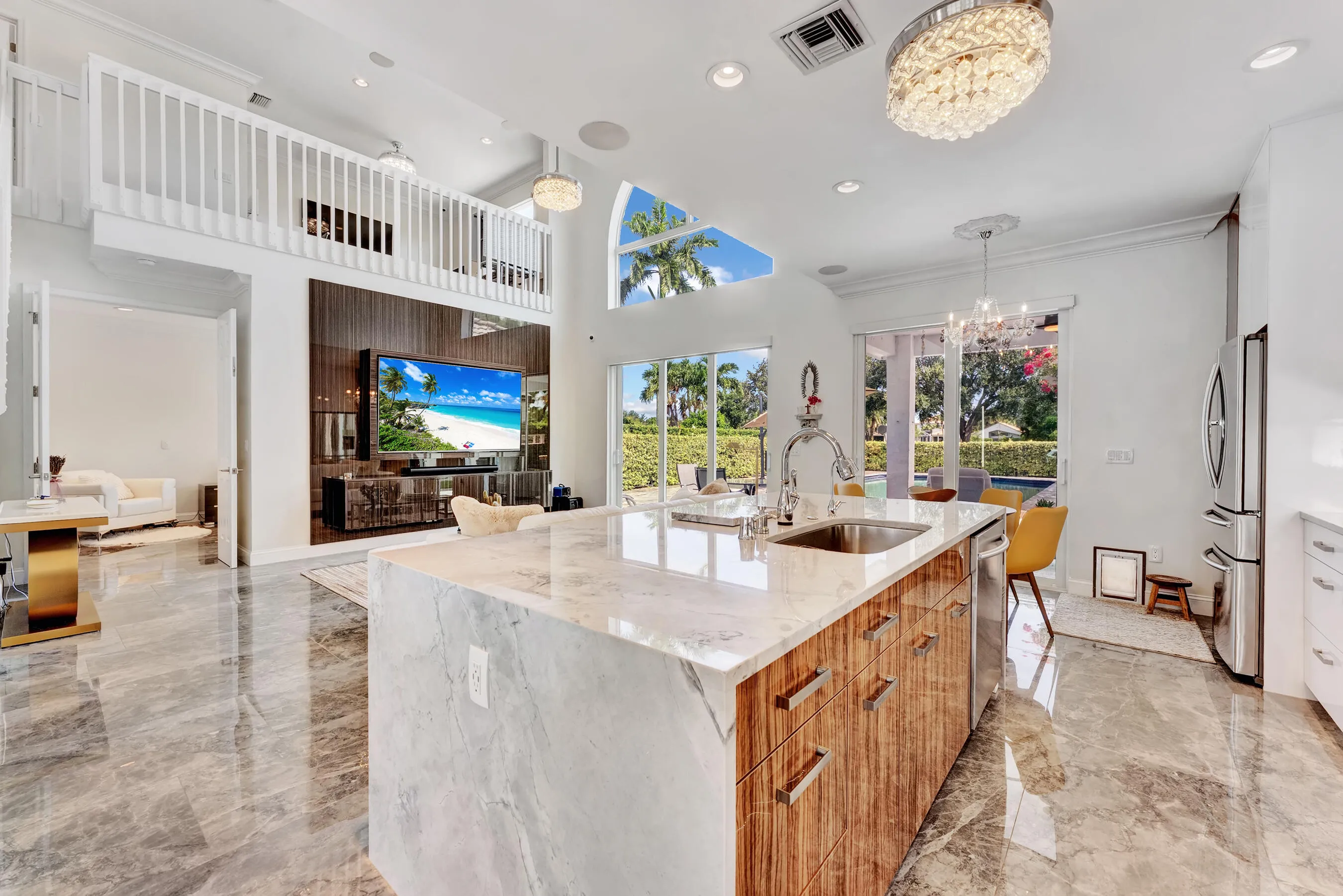 Open-concept great room and kitchen under soaring vaulted ceilings with arched clerestory windows and designer chandeliers.