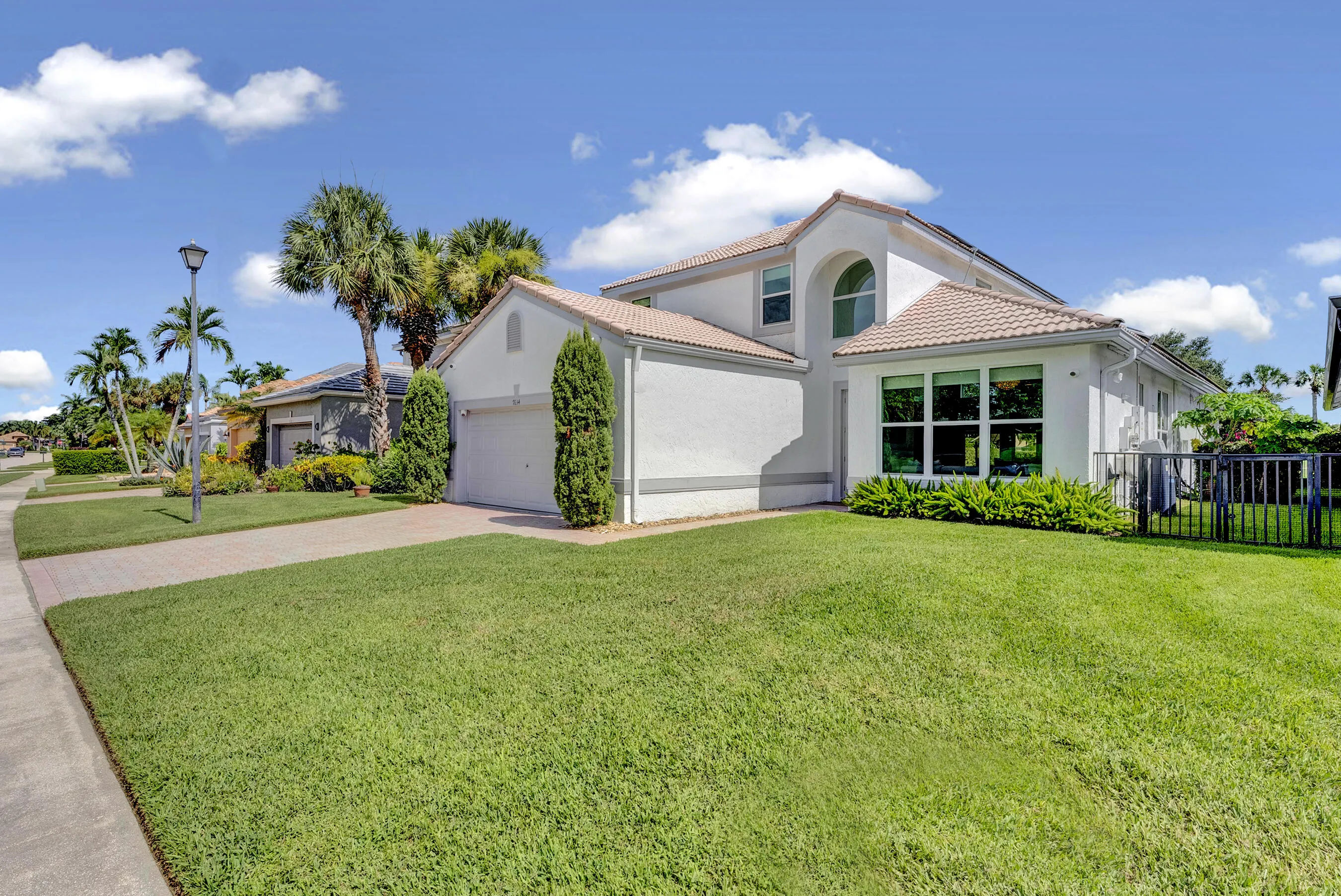 Corner view of the home's front exterior showing the arched window feature, tropical landscaping, and oversized green lawn.