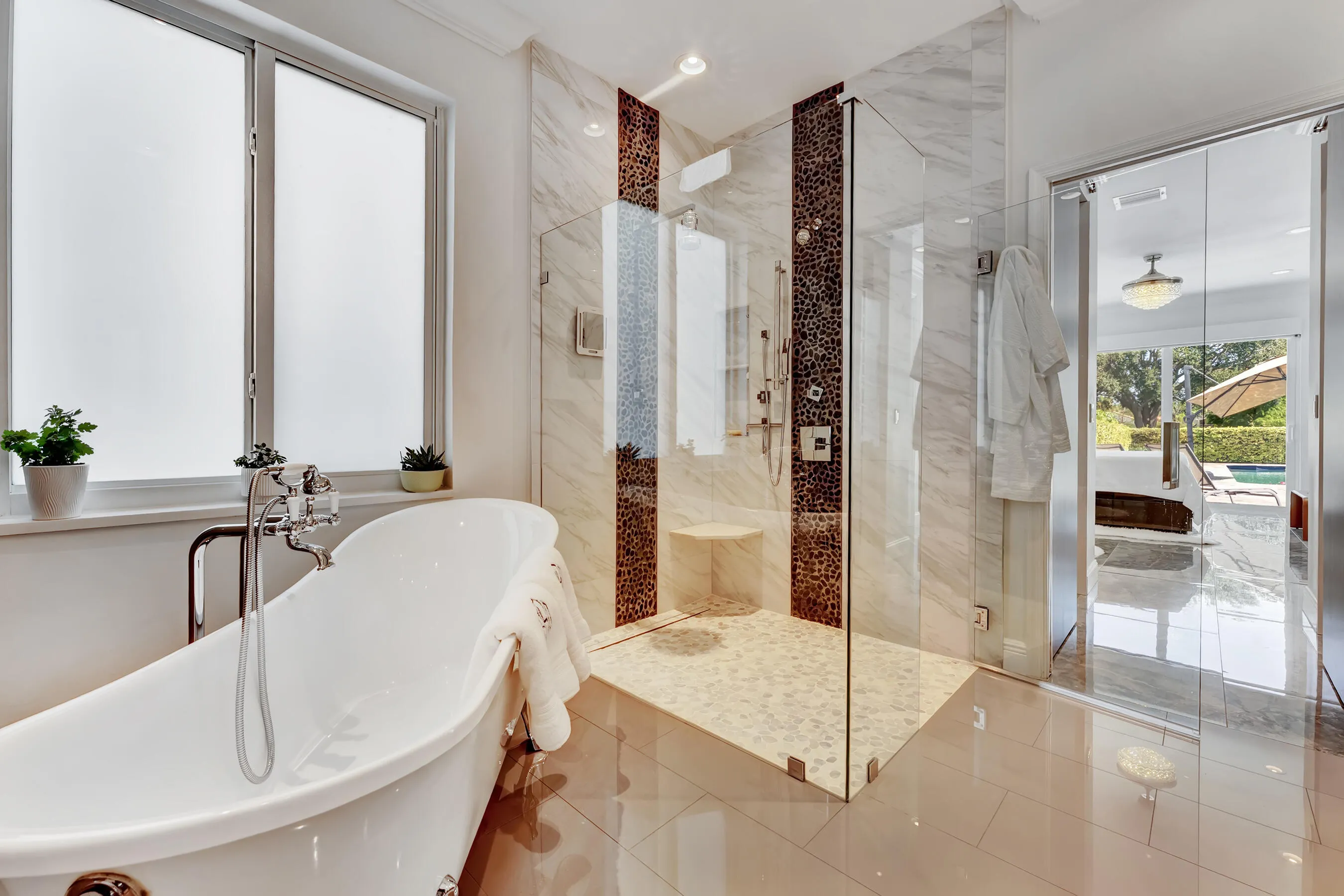 Freestanding clawfoot-style soaking tub beside an oversized frameless glass shower with rainfall fixtures and designer tile.
