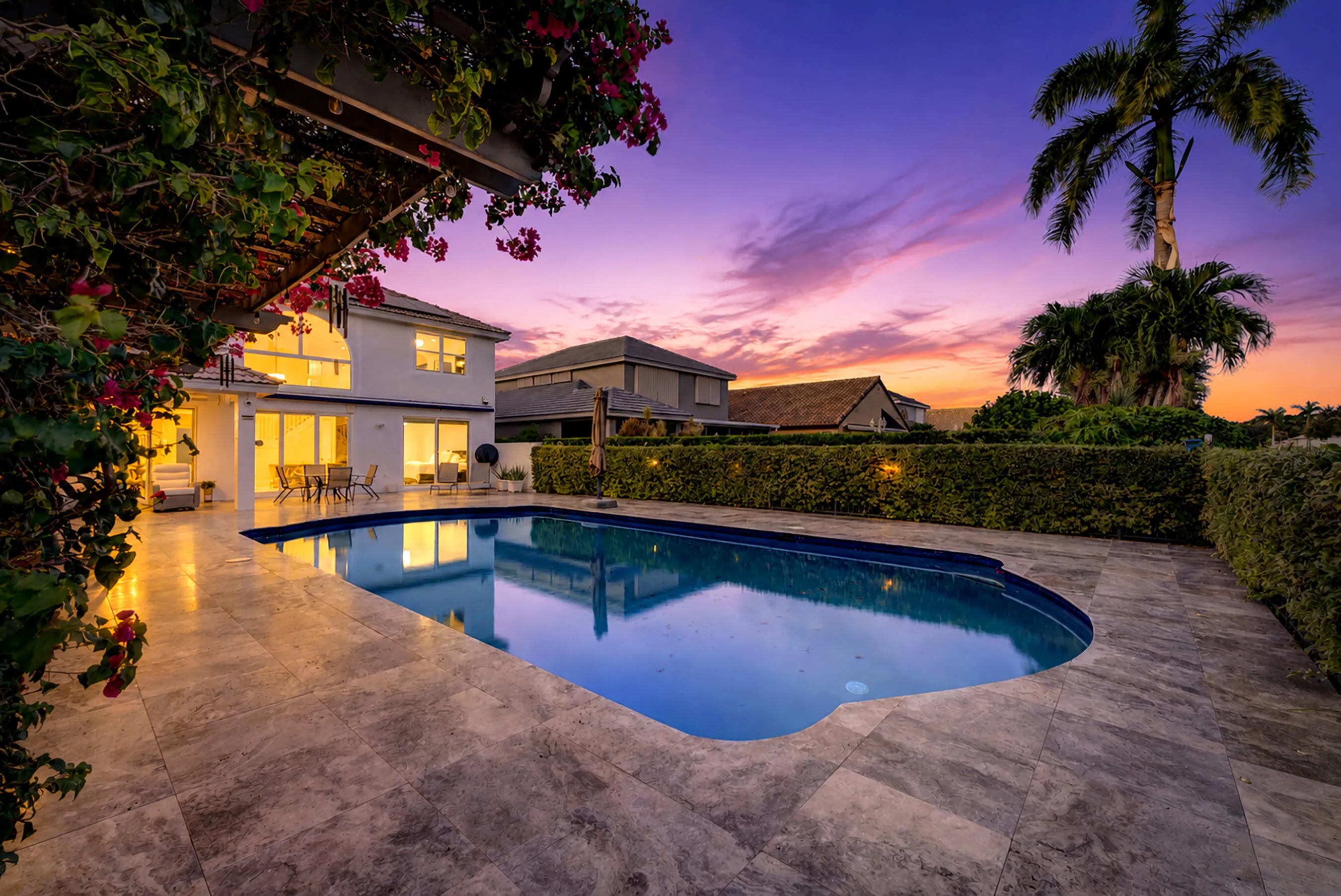 Pool at twilight with underwater lighting, purple-and-gold sunset sky, and towering royal palm.