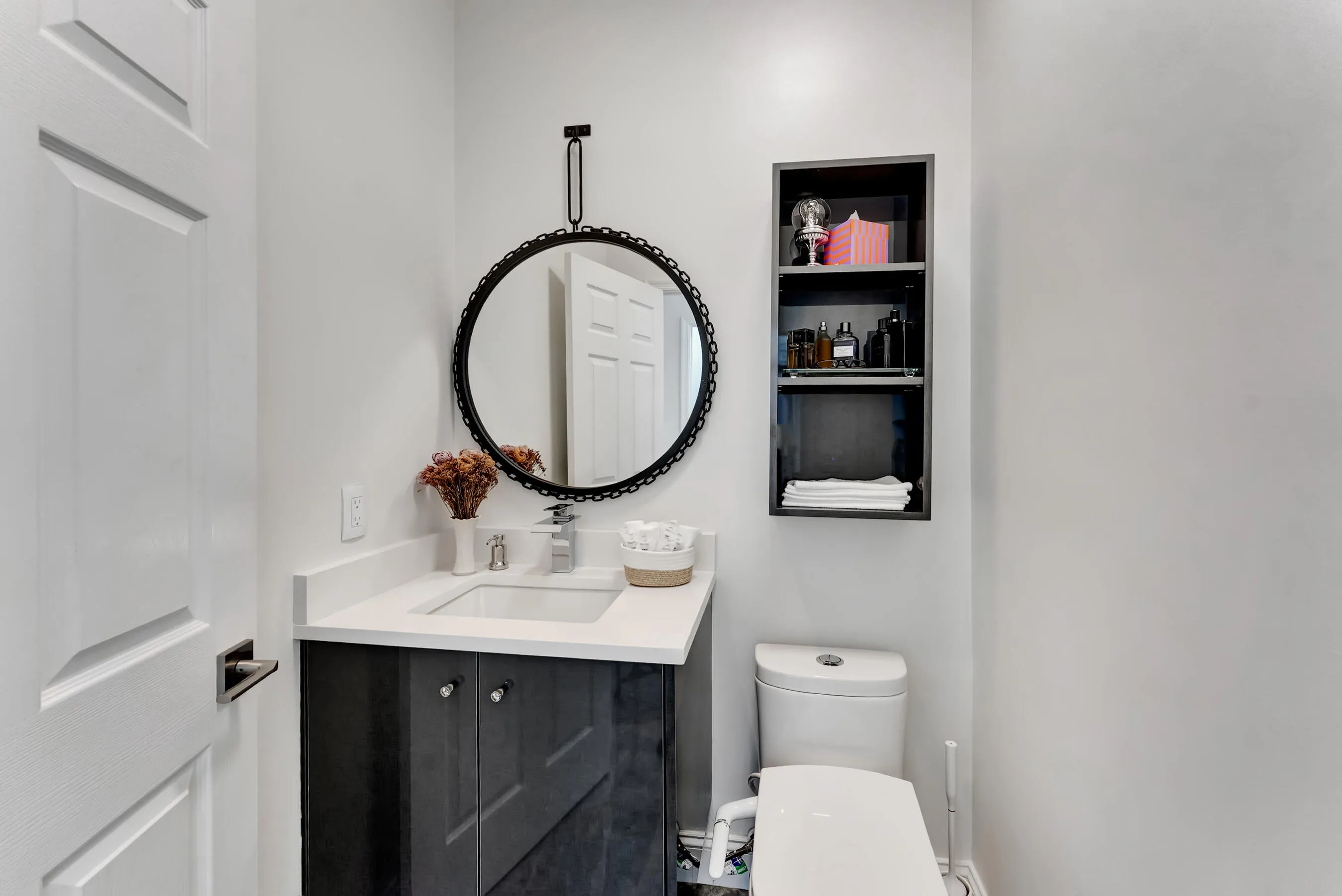 Stylish powder bath for downstairs guests with dark wood vanity, round accent mirror, and built-in shelving niche.