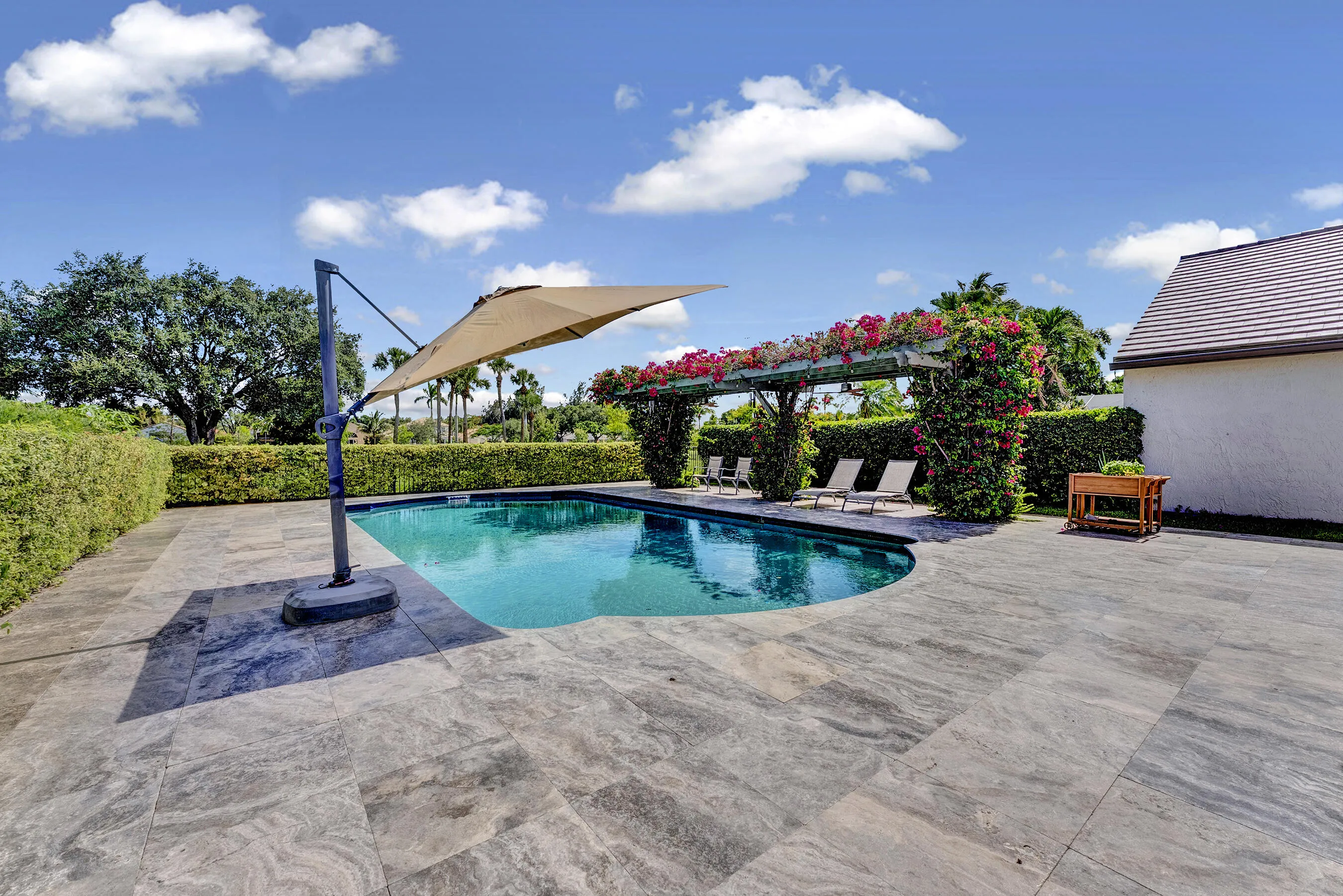 Sparkling private pool with cantilever umbrella, travertine deck, and lush green privacy hedges.
