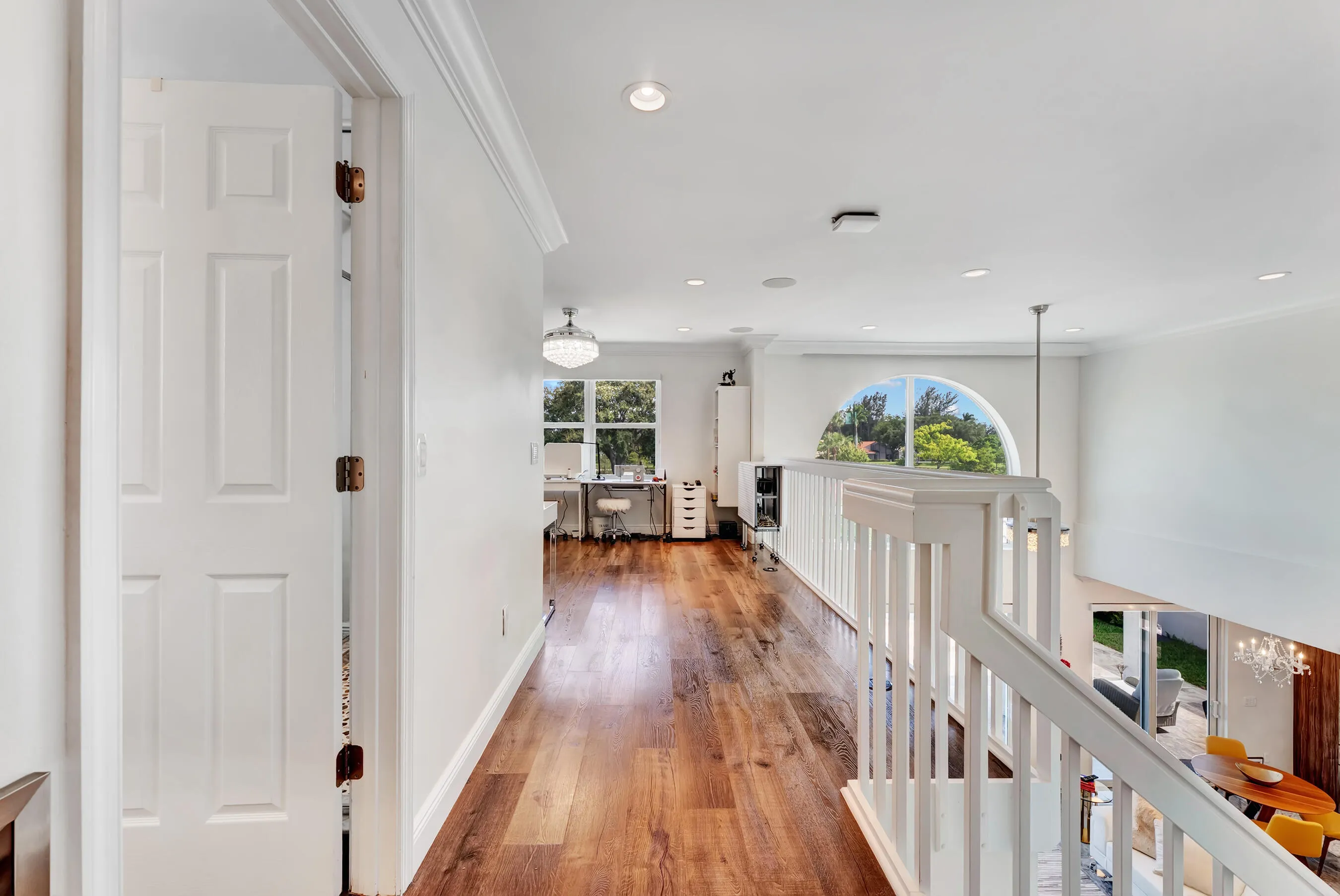 Upstairs landing with rich wood floors, white railing, and arched picture window.