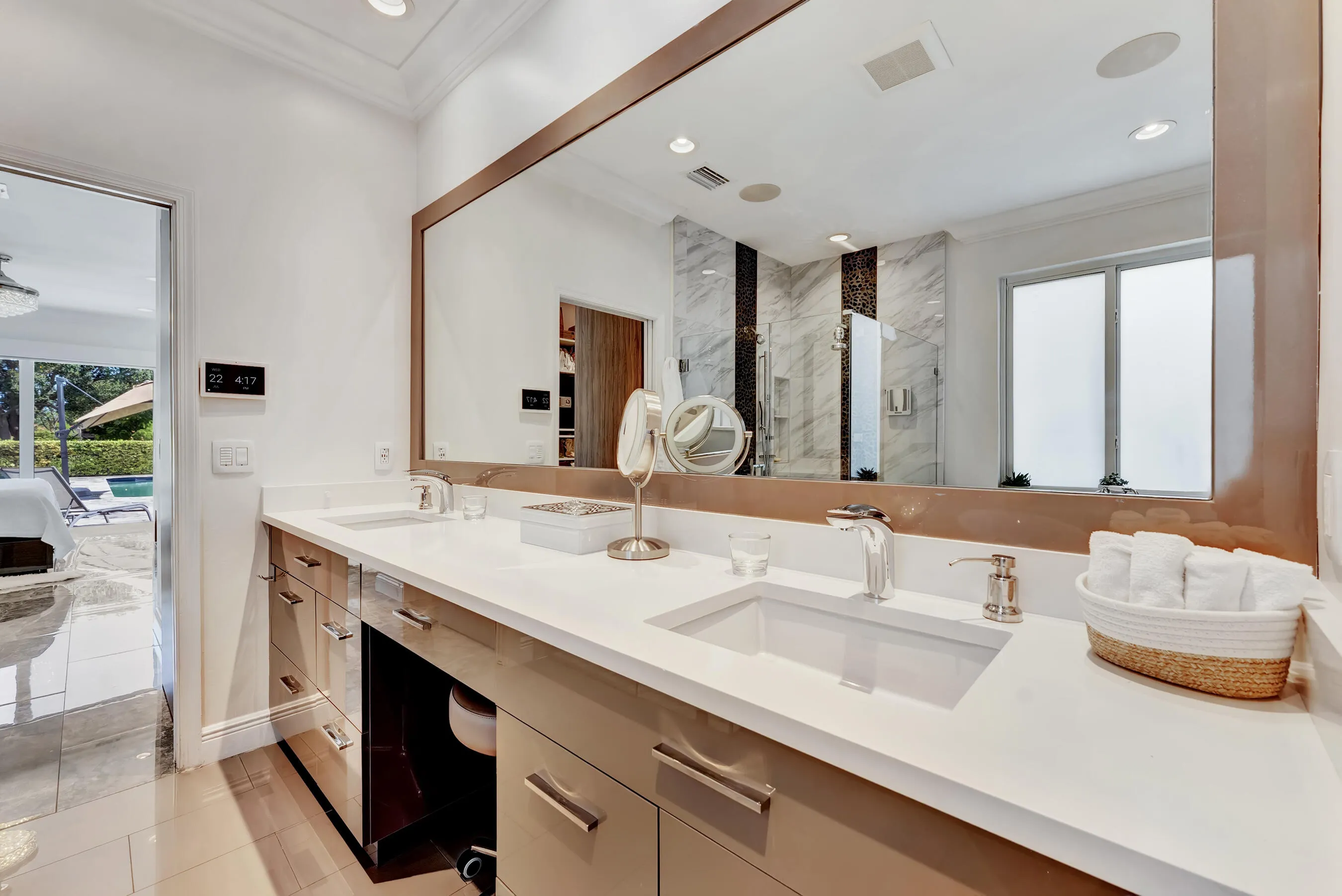 Primary bath vanity with quartz countertop, oversized framed mirror, and seated makeup station.